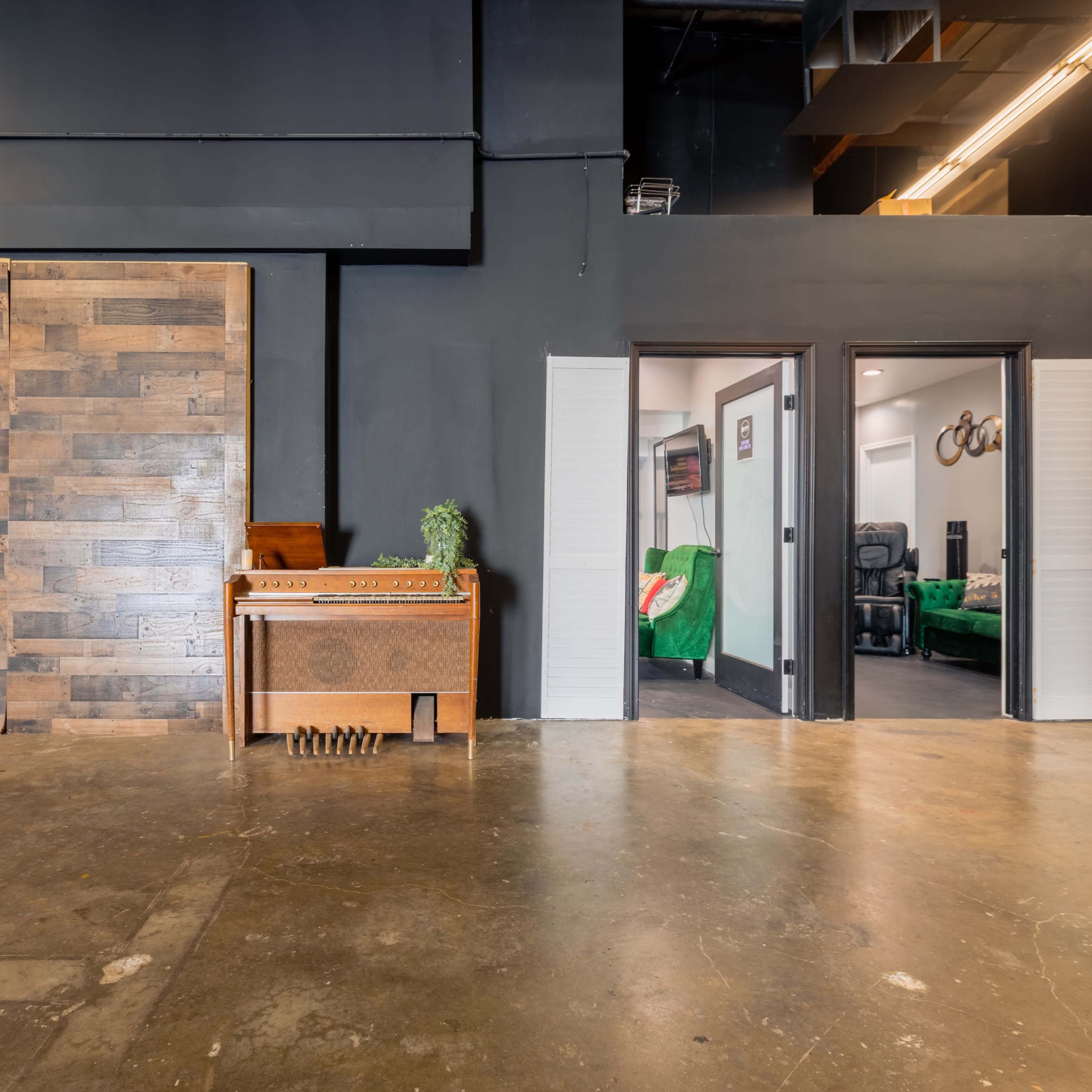 A studio space featuring a wooden wall, a vintage piano, and two doorways leading to separate rooms with green furnishings.