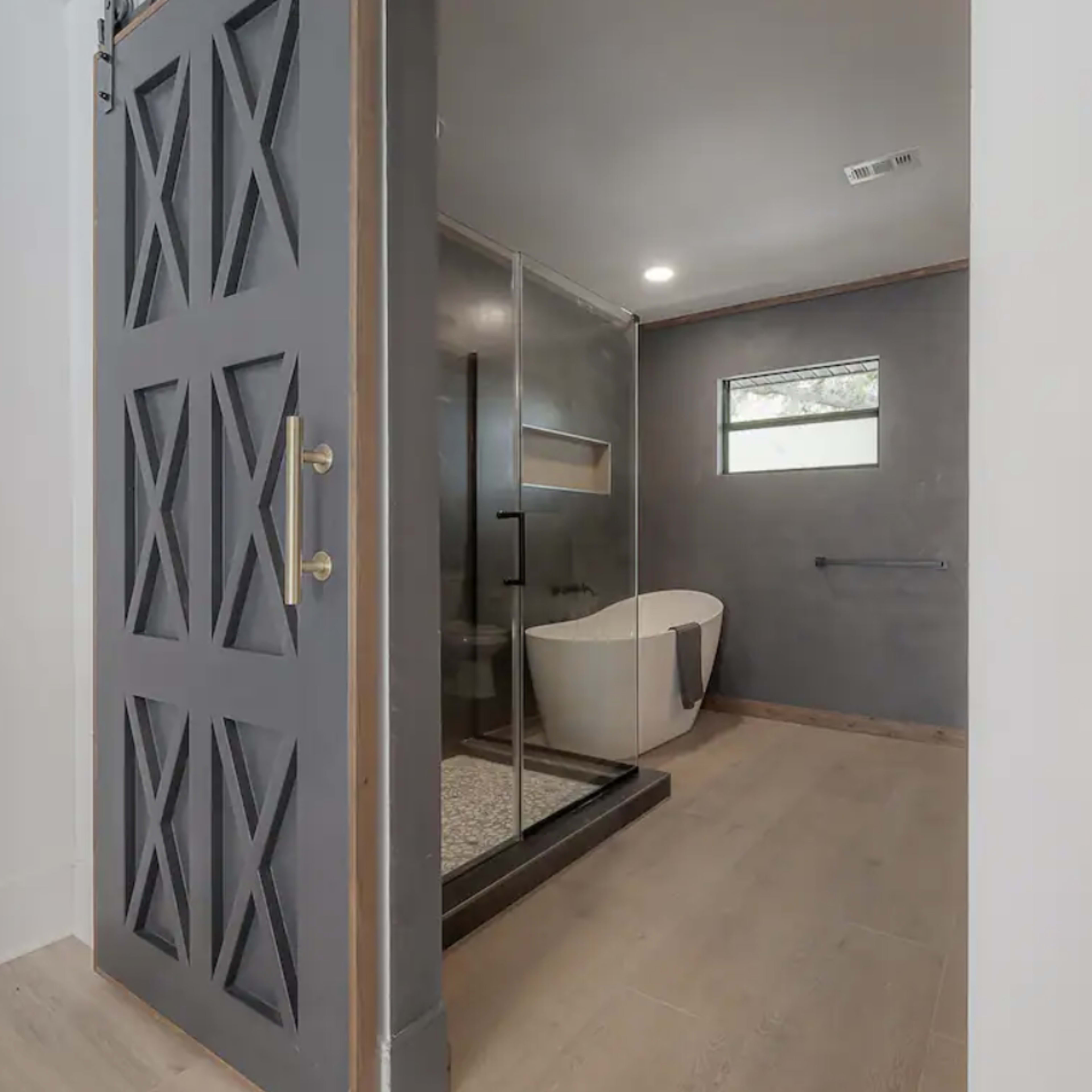 A modern bathroom features a glass shower enclosure and a freestanding bathtub, with a door leading into the space.