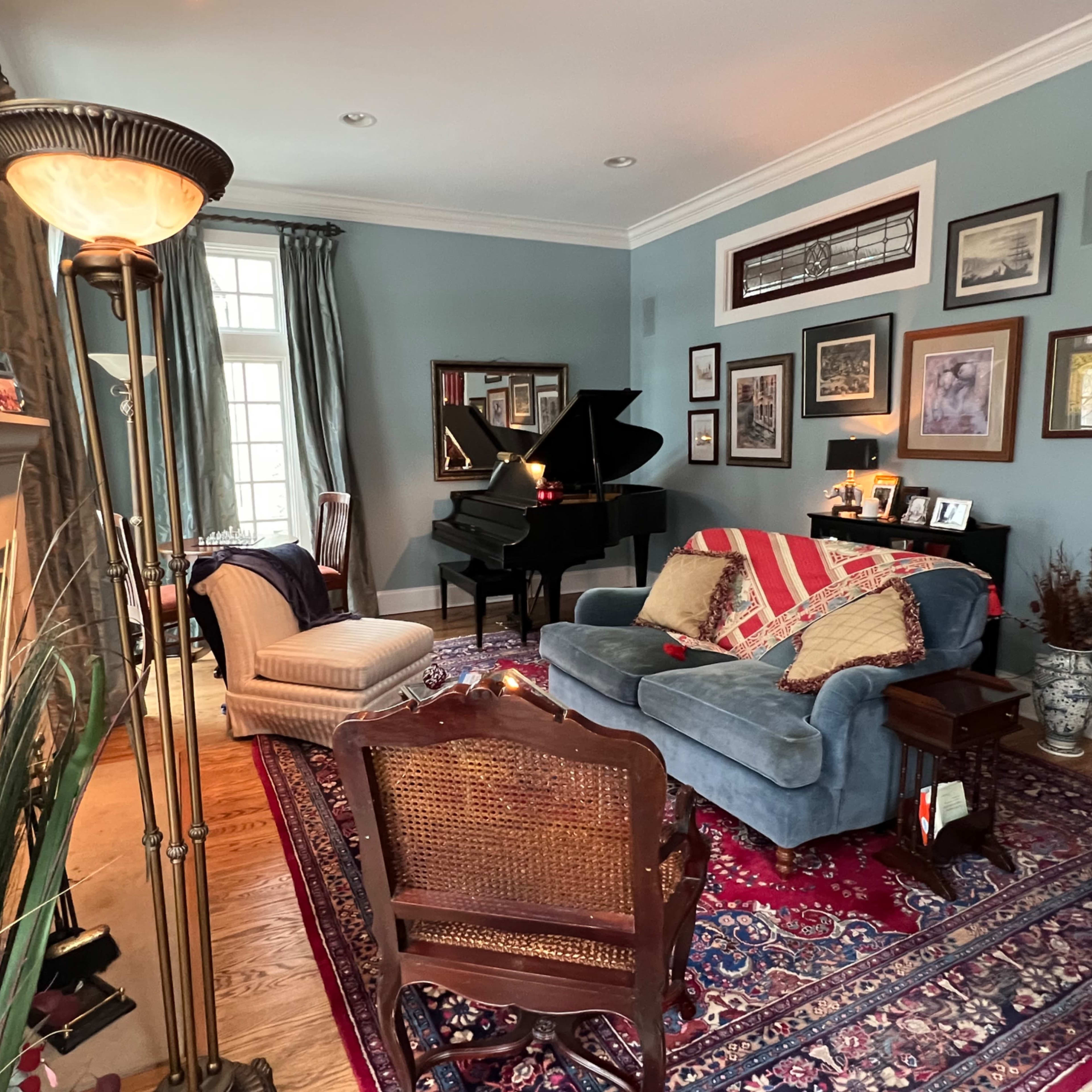 A cozy living room featuring a grand piano, a blue couch with striped pillows, and various framed artworks on the walls.