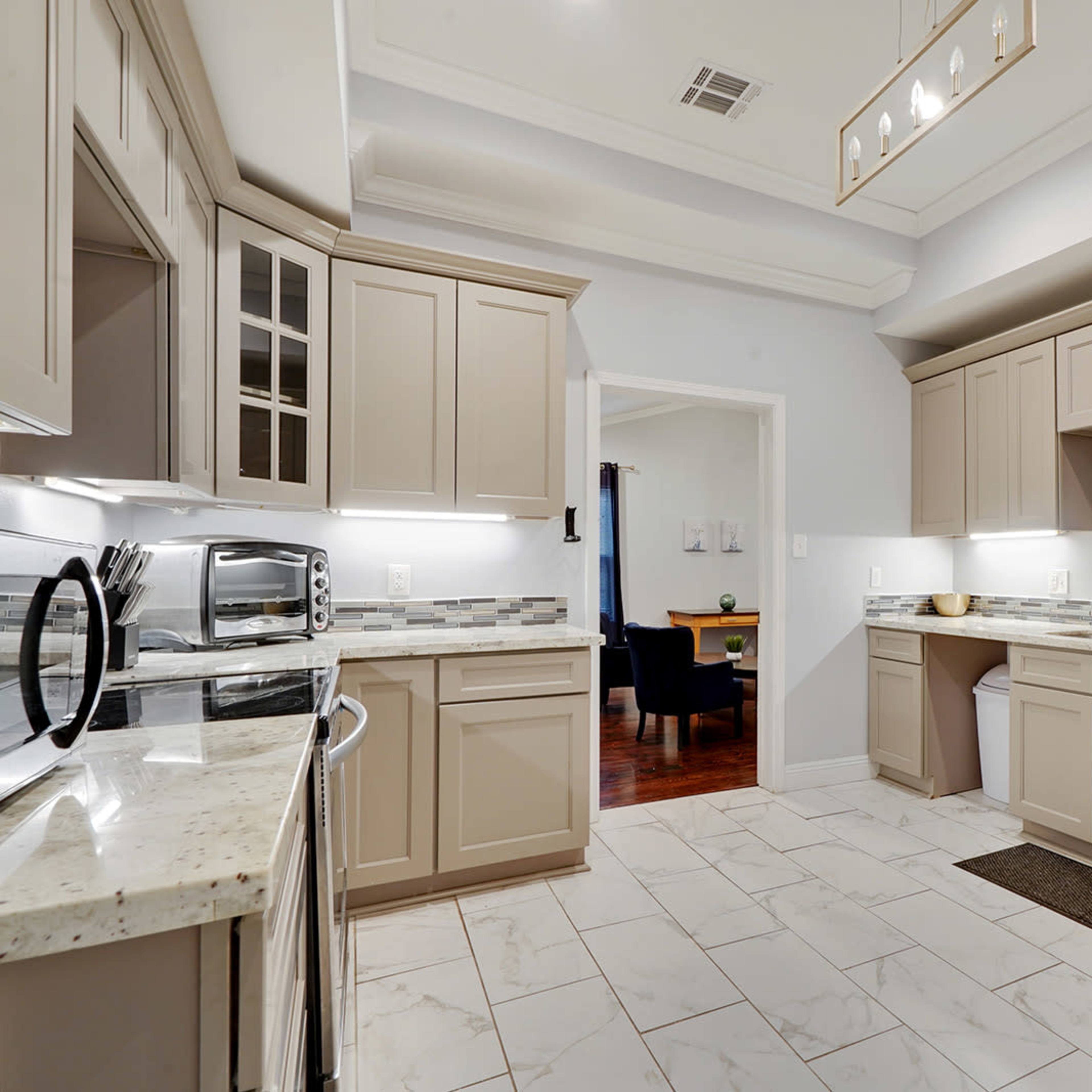 A modern kitchen with beige cabinetry, stainless steel appliances, and light-colored stone countertops.