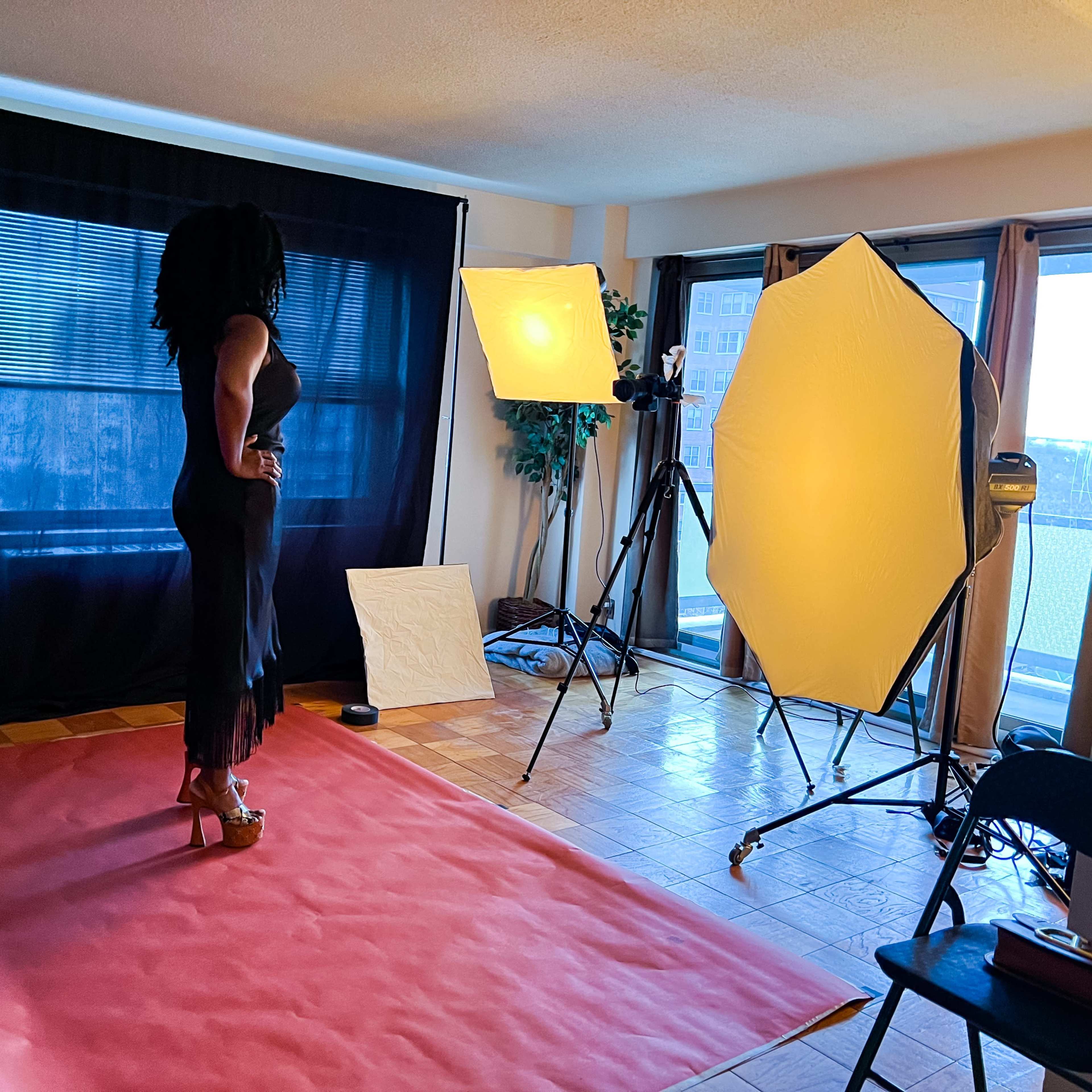 A woman poses on a red carpet in a studio set up with bright lighting and a black backdrop.