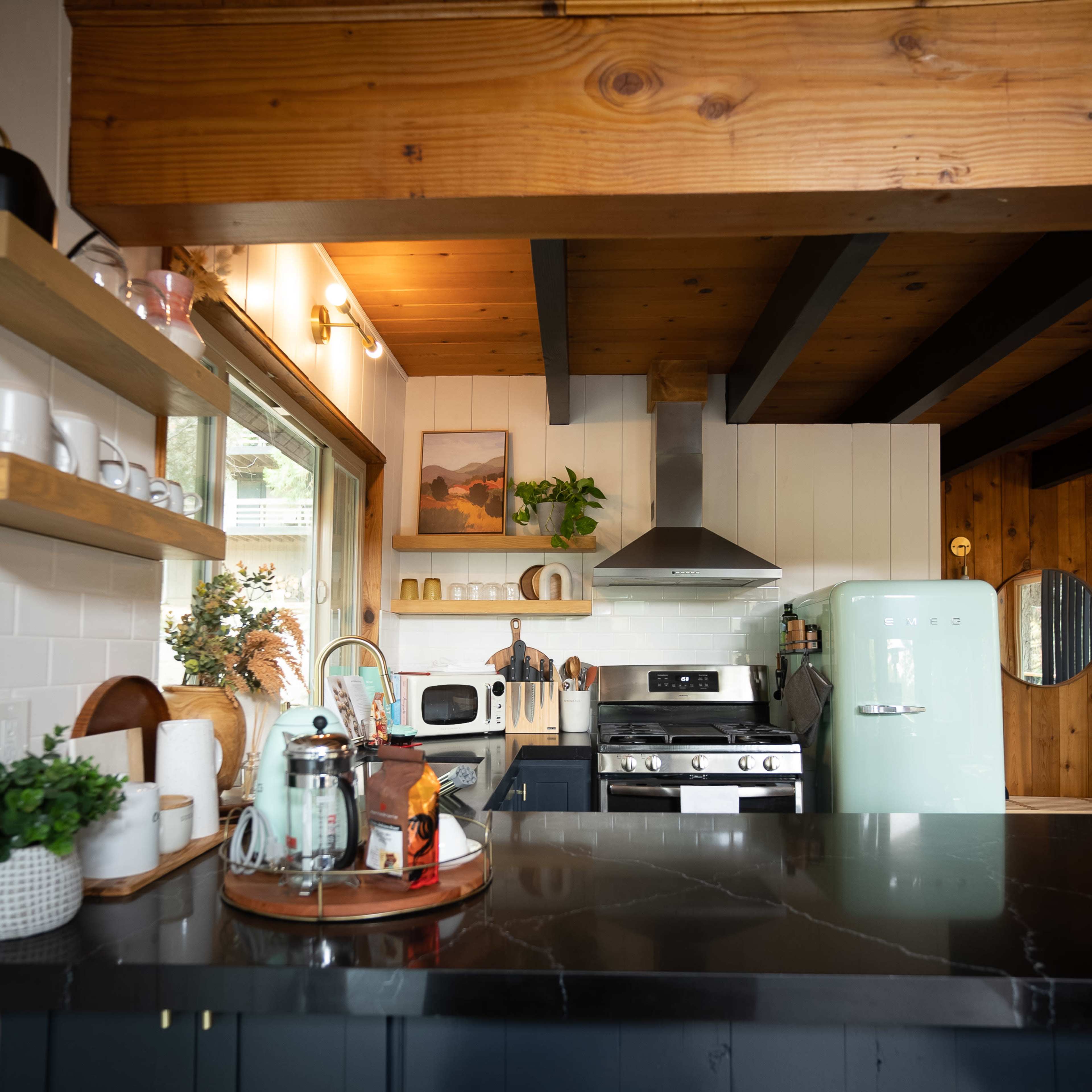 A modern kitchen features wooden beams, a green retro refrigerator, and stainless steel appliances, with a table set for coffee.