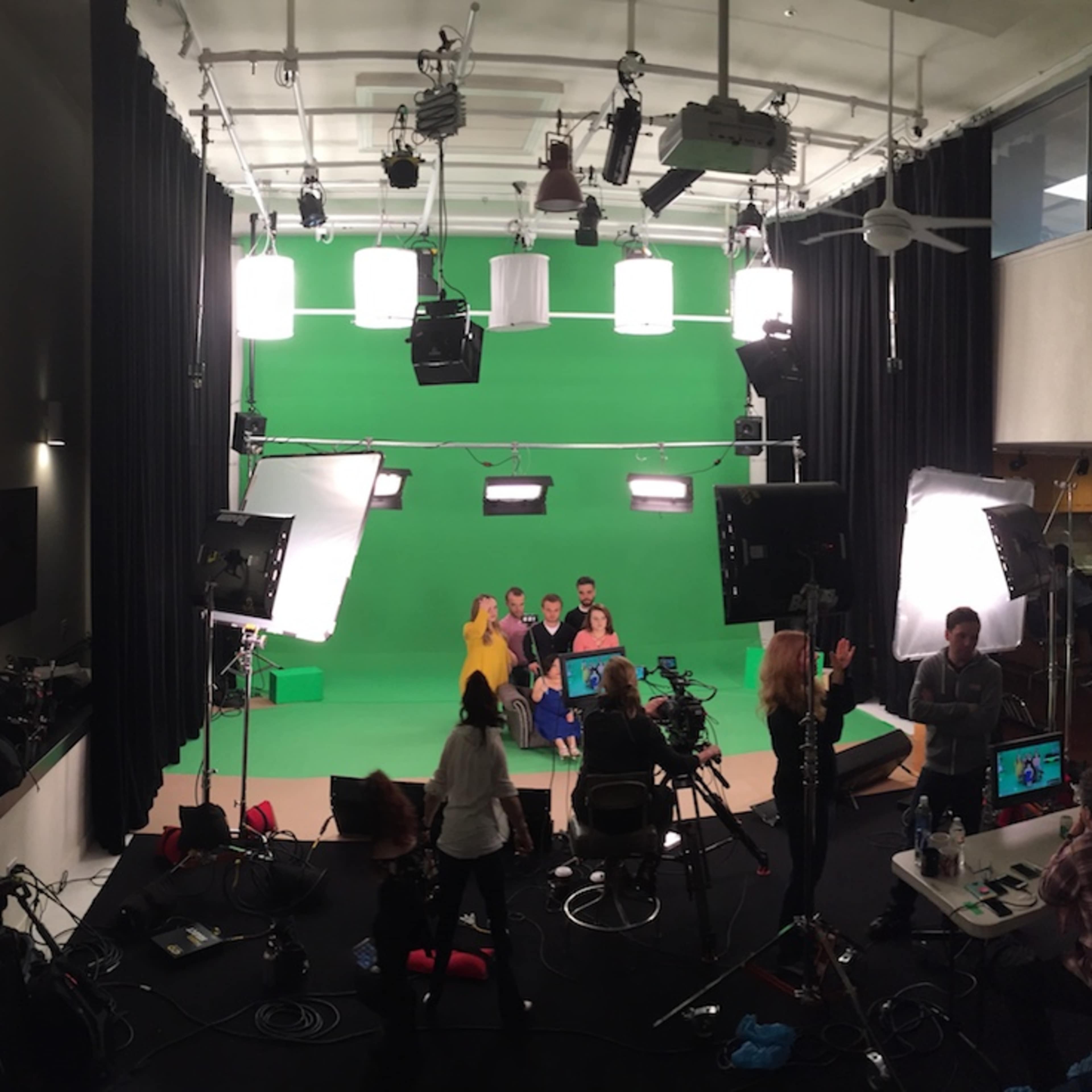 A film studio is set up for a shoot with multiple cameras, lighting equipment, and a green screen.