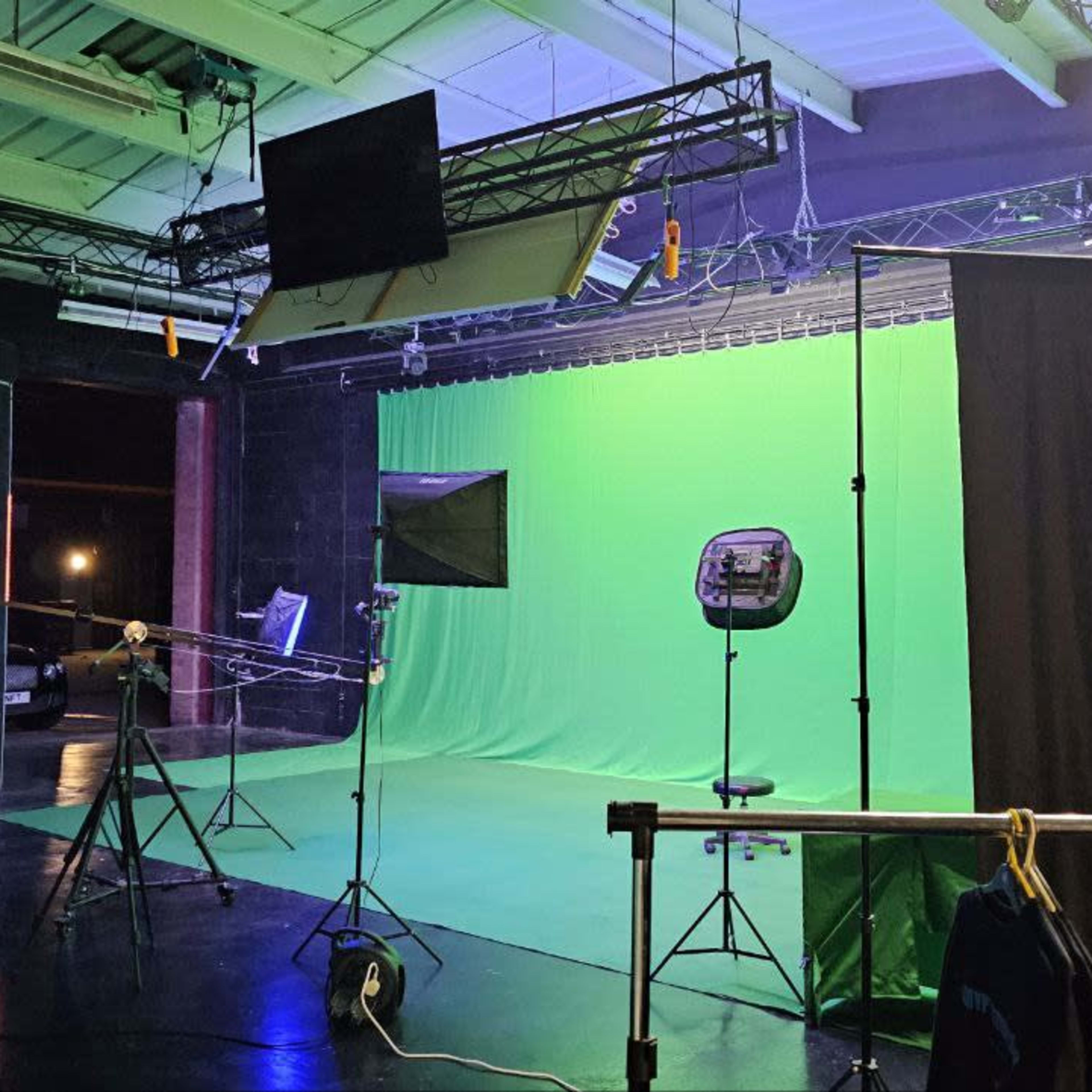 A film studio setup with a green screen background, lighting equipment, and various supports for filming.