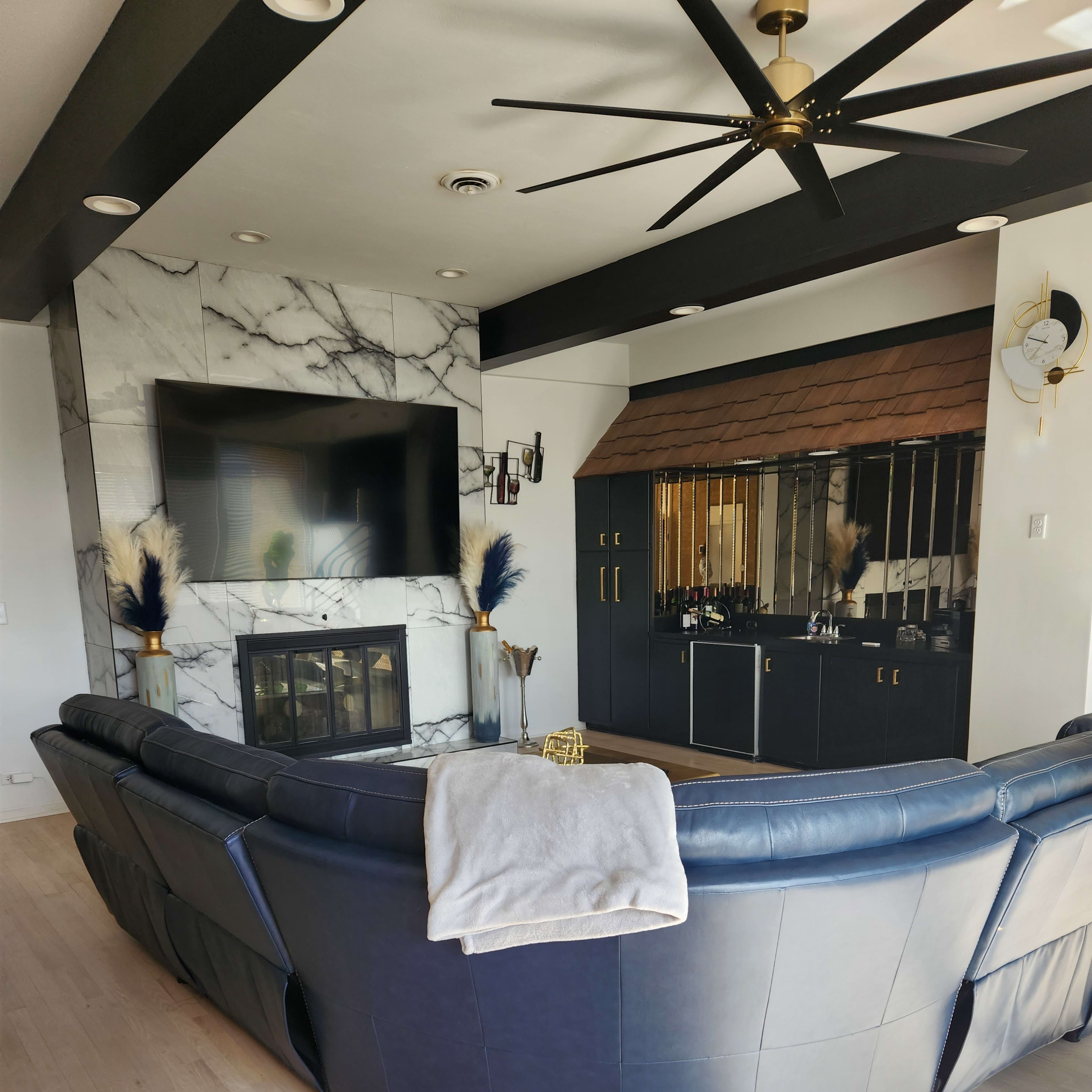 A modern living room featuring a large sectional sofa, a marble fireplace, and a dark cabinetry bar area with a large mirror.