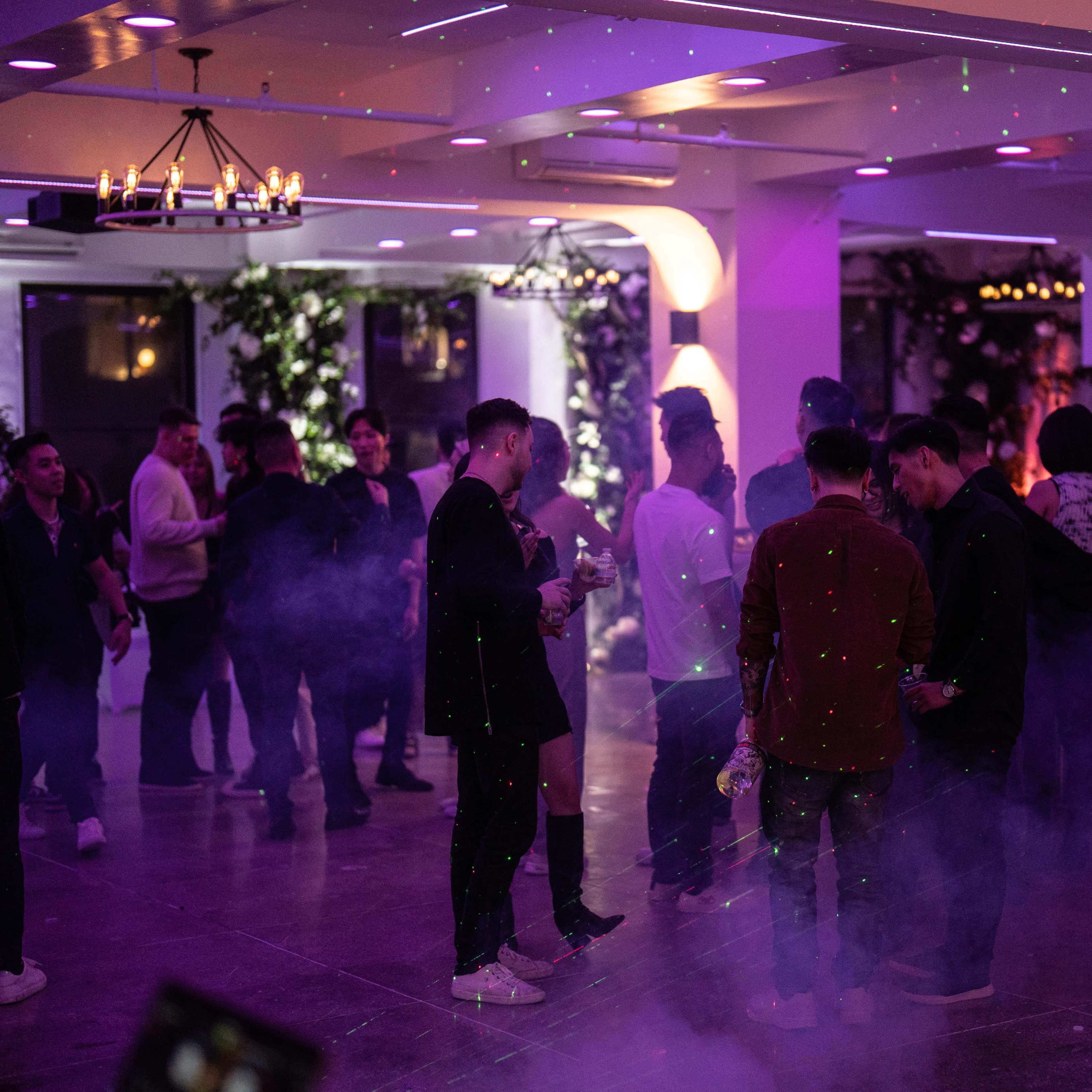 A group of people socialize in a dimly lit event space filled with purple lighting and fog effects.