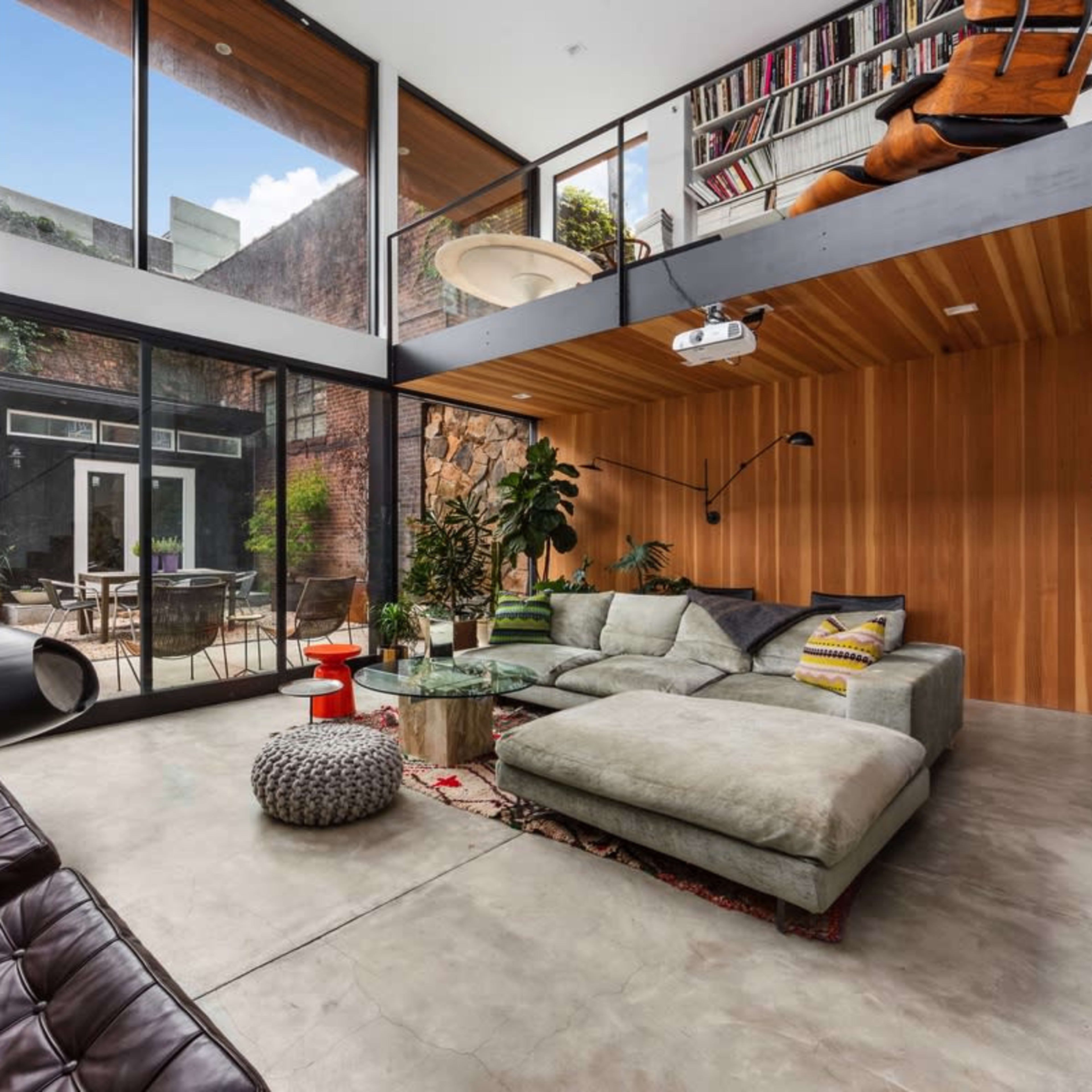 A modern living room featuring large glass windows, minimalistic furniture, and an open loft area with a staircase.