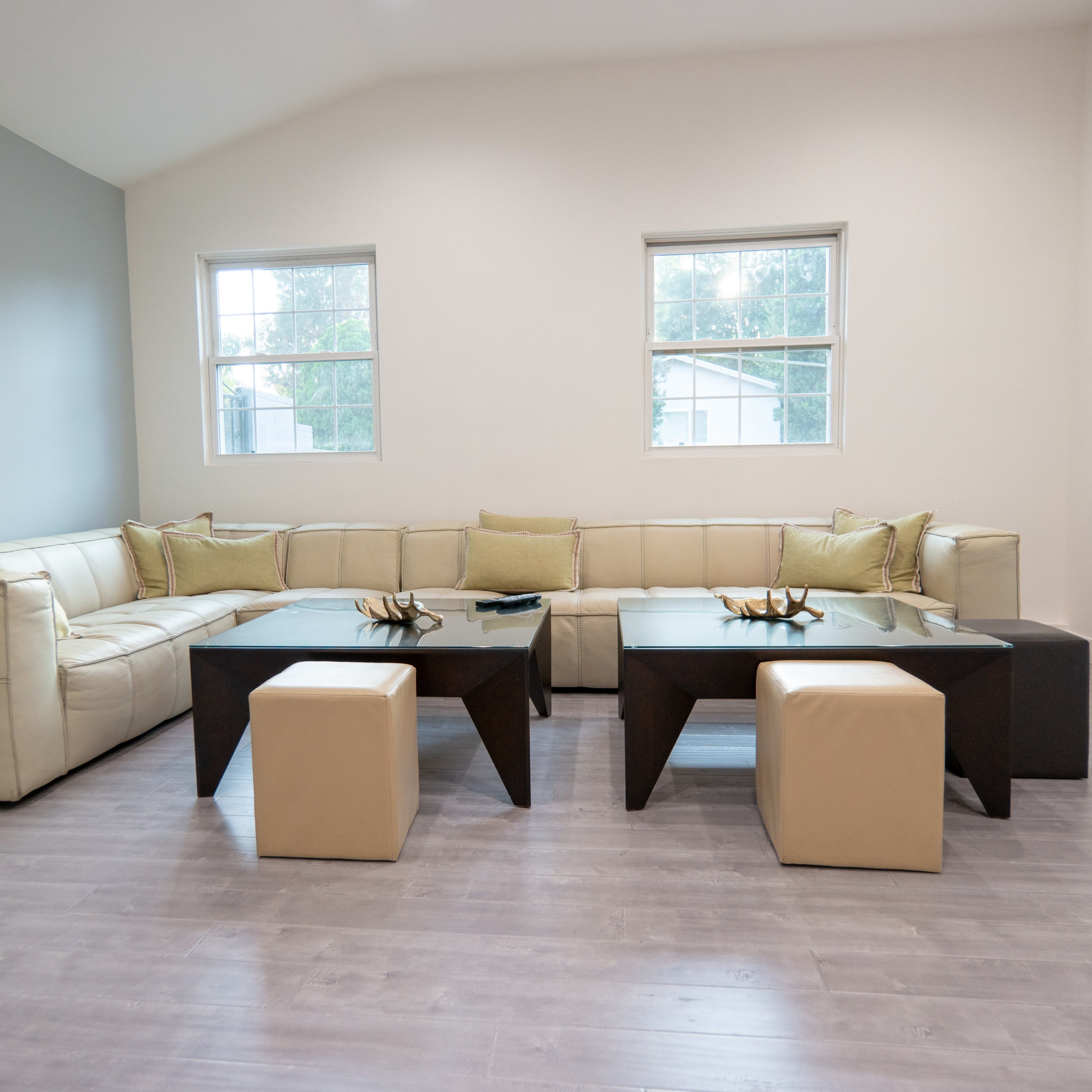 A modern living room featuring a large beige sectional sofa, two black coffee tables, and light gray walls with large windows.