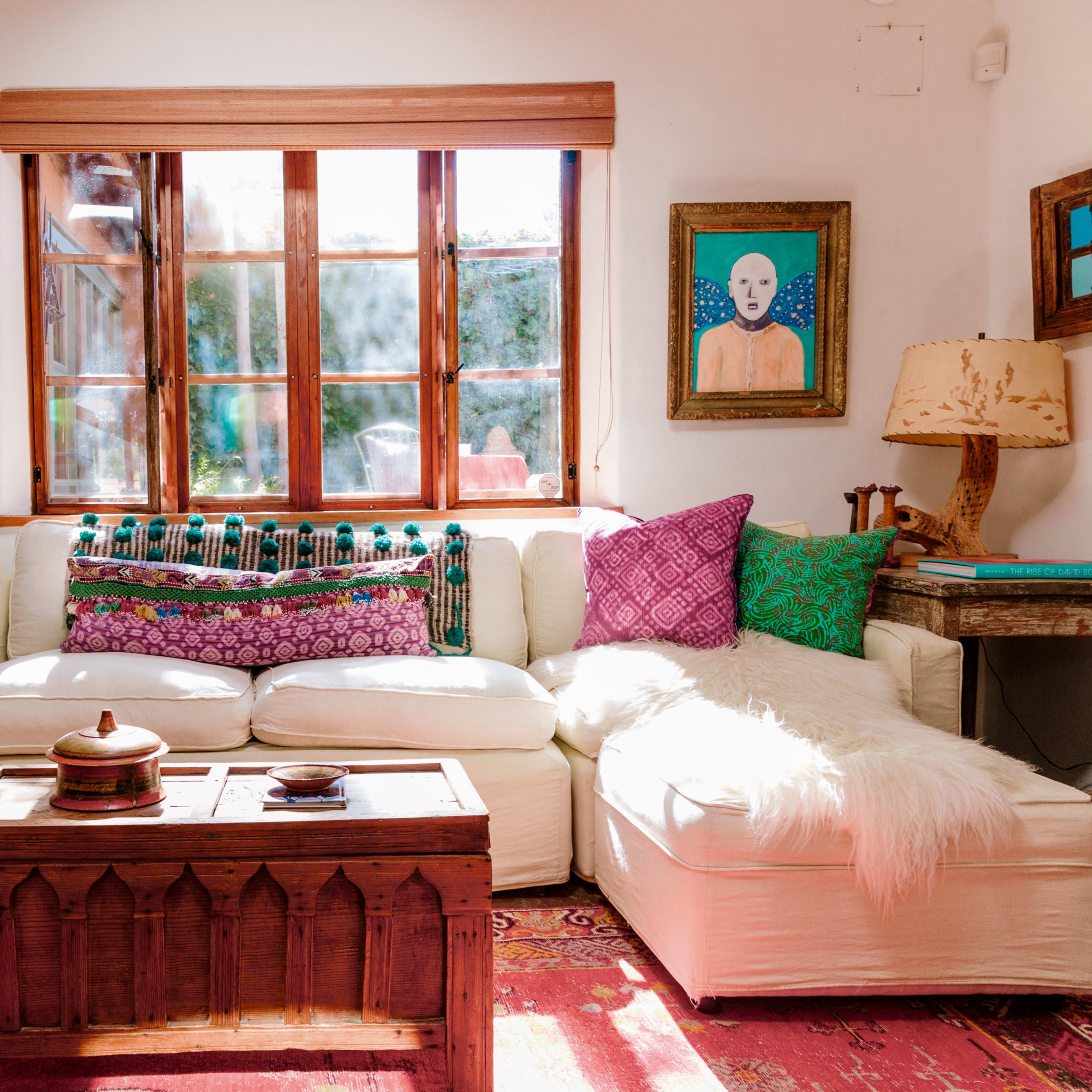 The scene shows a bright living room featuring a white sectional sofa adorned with colorful cushions and a wooden coffee table in front.