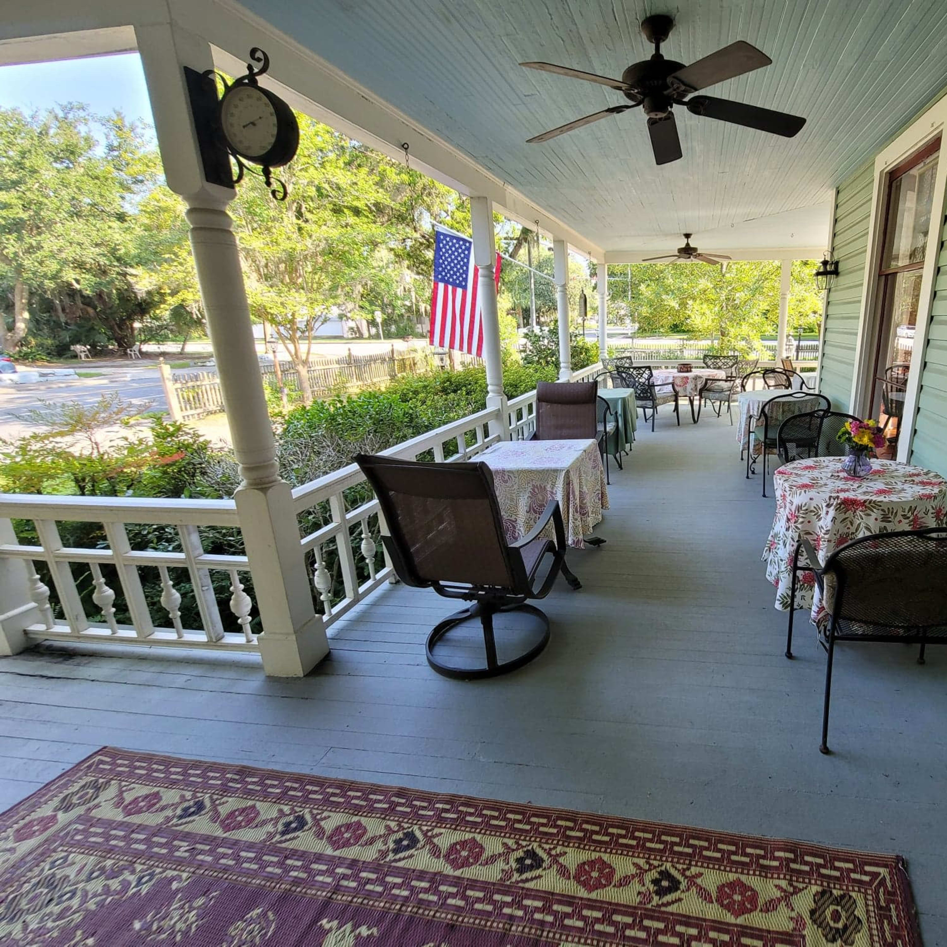 A porch with several tables and chairs, decorated with patterned tablecloths, and an American flag hanging prominently.