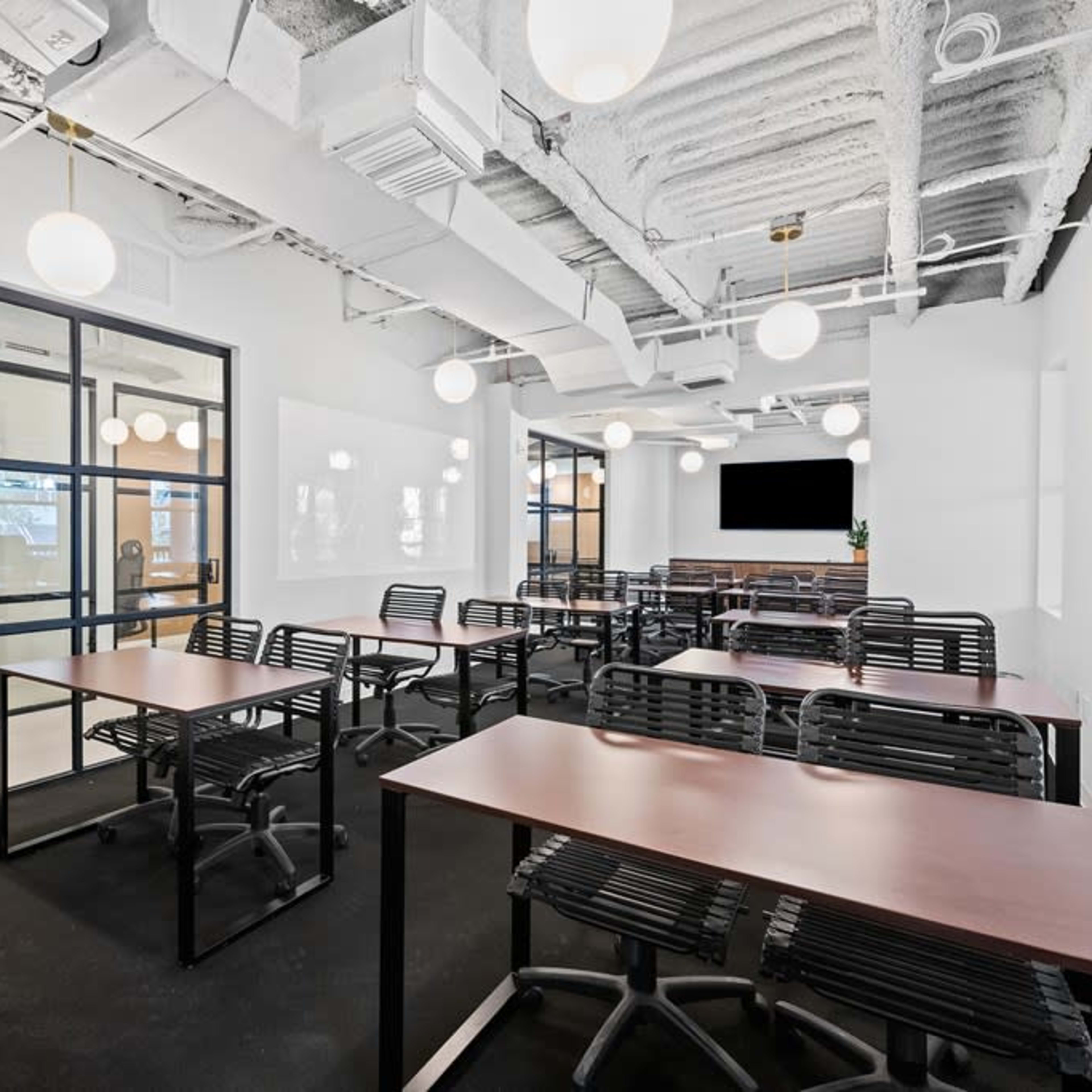 A modern office space with several black chairs and wooden tables arranged in a layout suitable for meetings or collaborative work.