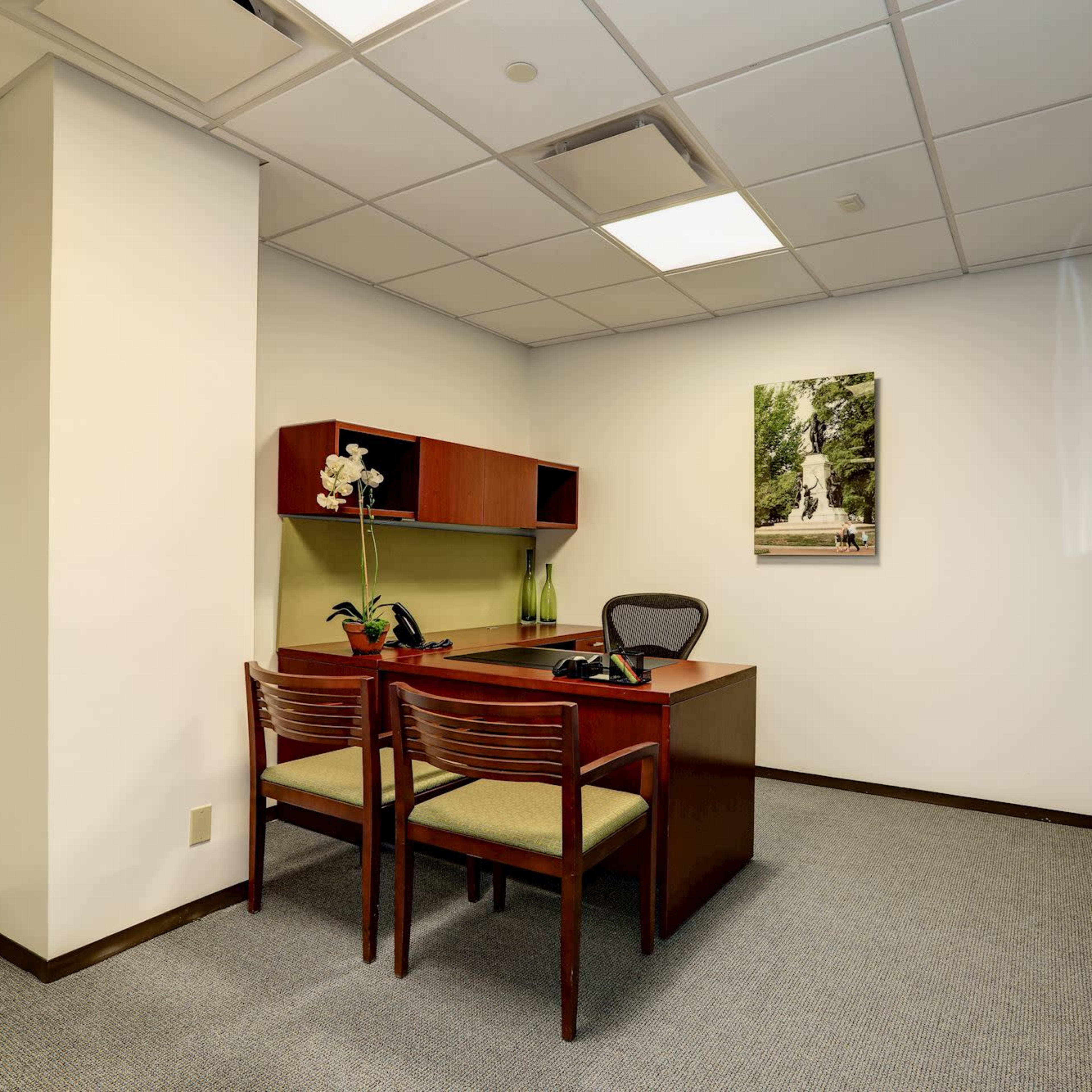A small, modern office with a desk, two chairs, and a wall-mounted artwork.