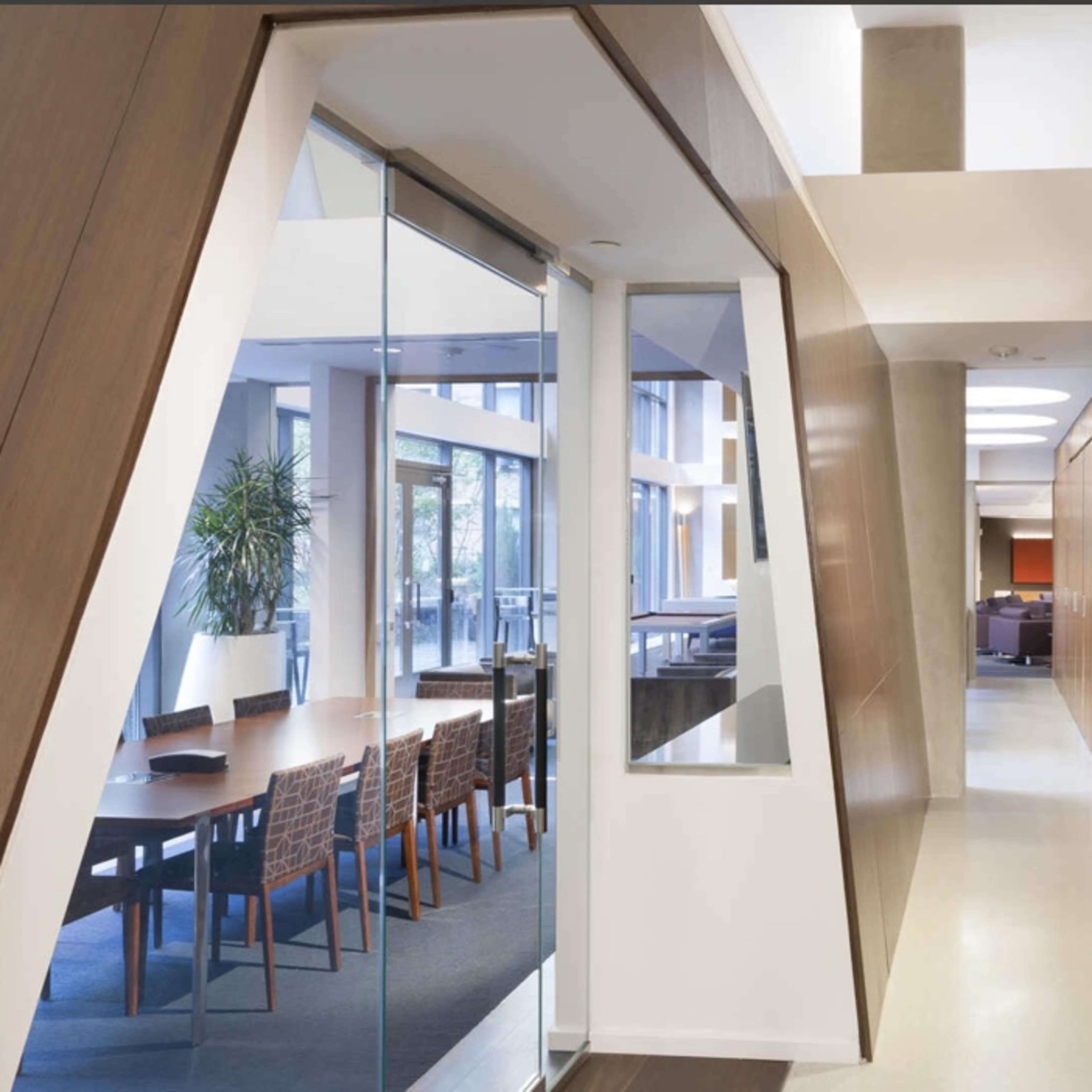 A modern office corridor leading to a glass-walled conference room on one side and wooden-paneled walls on the other.
