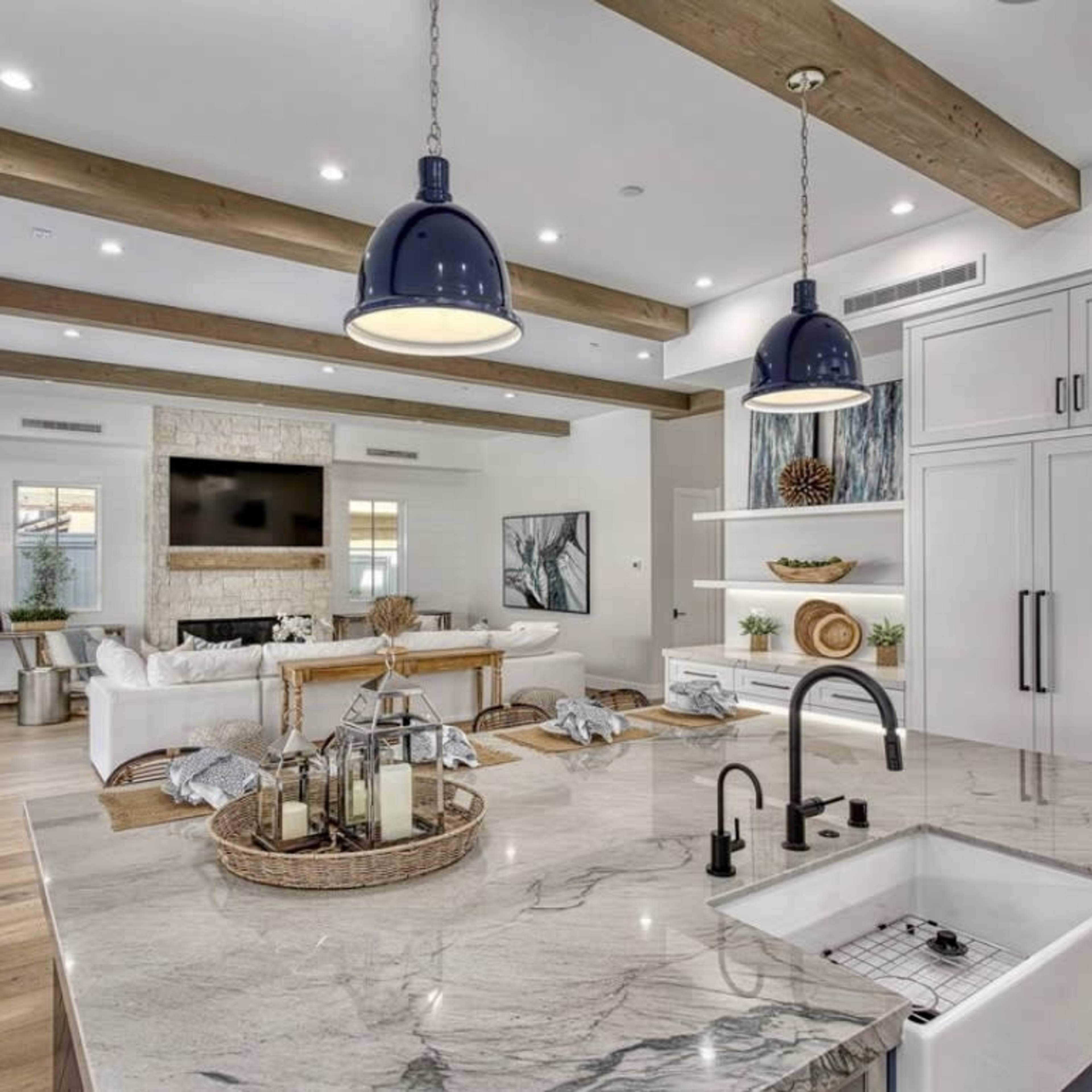 A modern kitchen opens into a living area with wooden beams, a large TV, and a sliding door leading to an outdoor space.