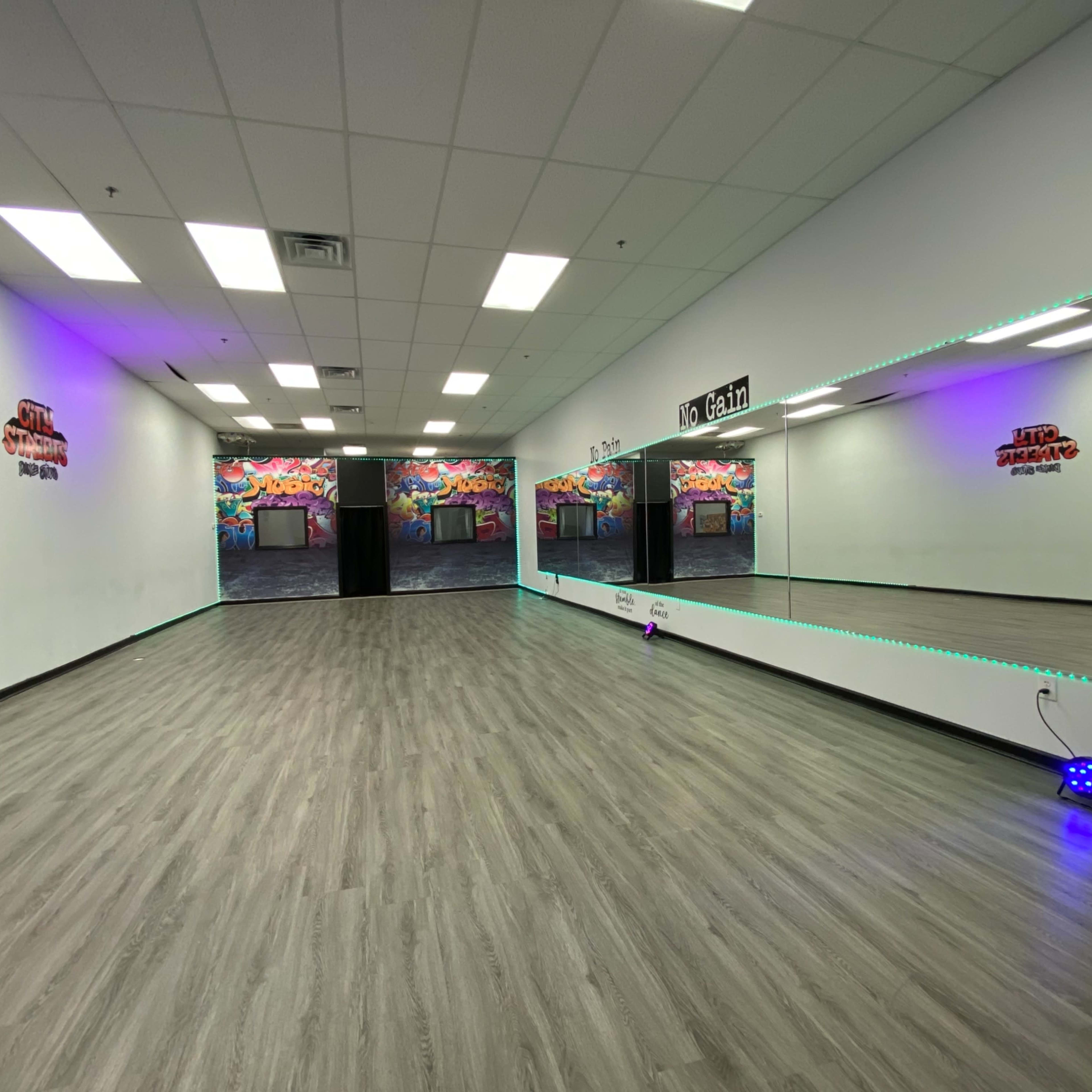 A spacious dance studio with mirrored walls and colorful mural artwork in the background.