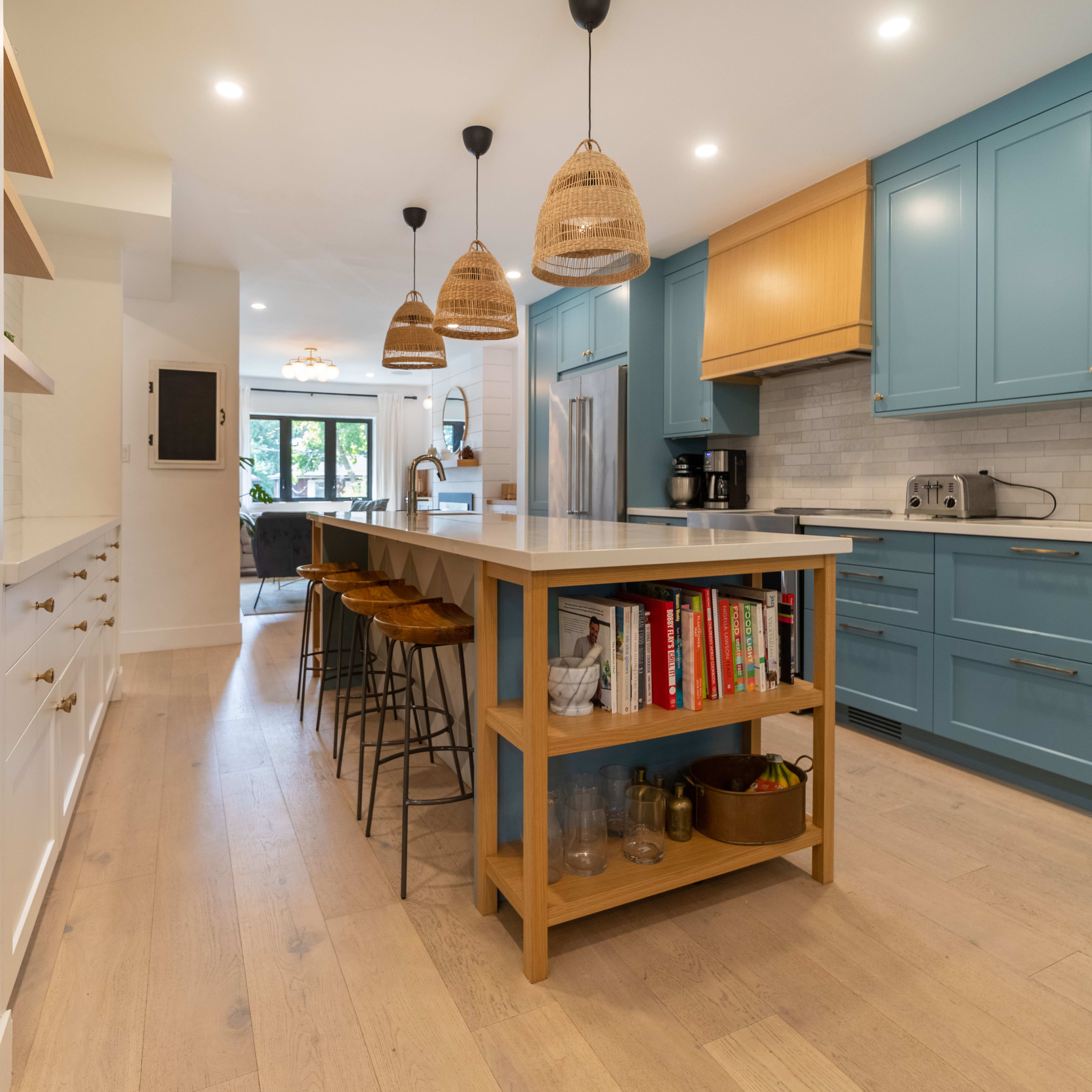 A modern kitchen featuring blue cabinetry, a central island with a light wood base, and three woven pendant lights hanging above.