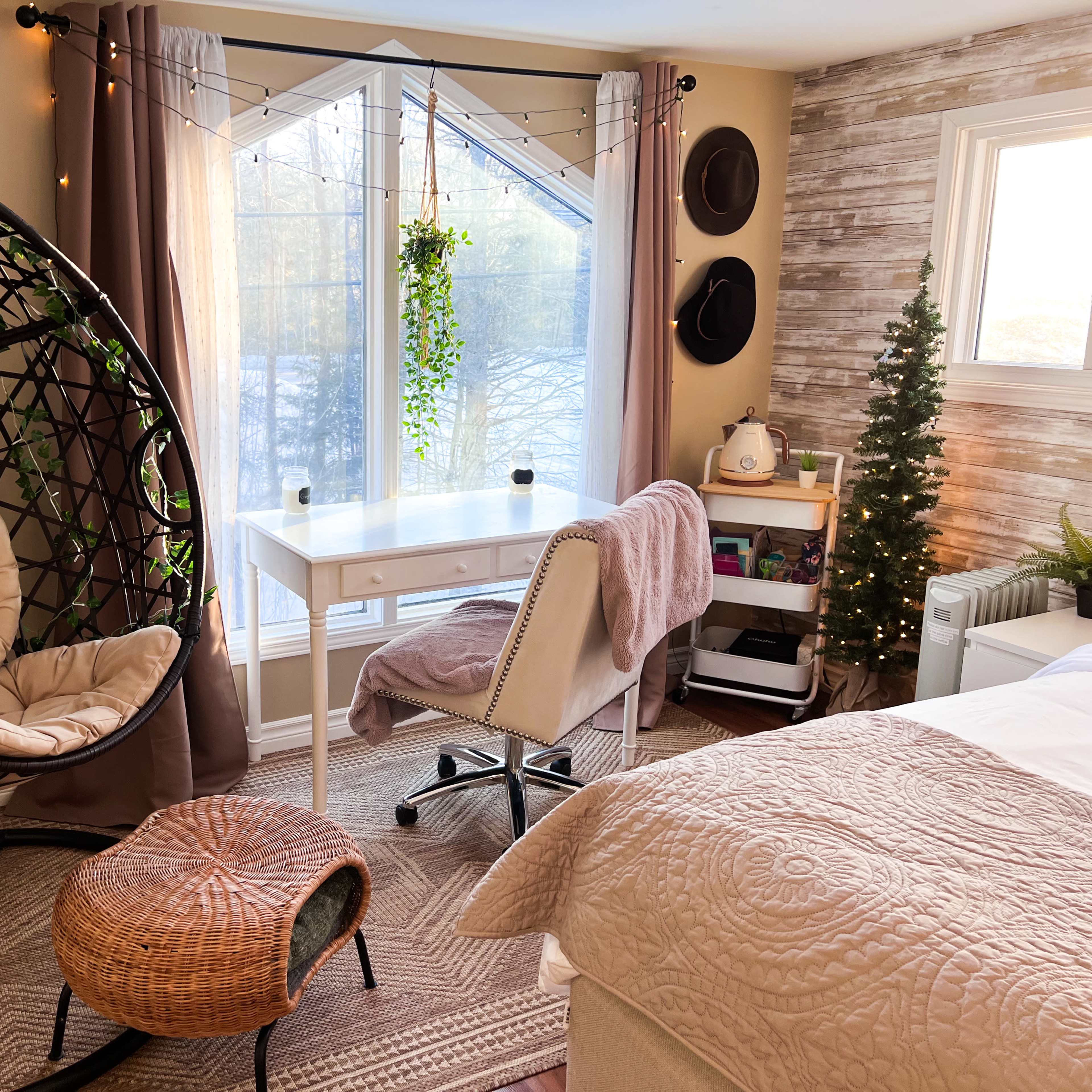 A cozy room featuring a hanging chair, a desk with a chair, and a small tree, all arranged near a large window with natural light.