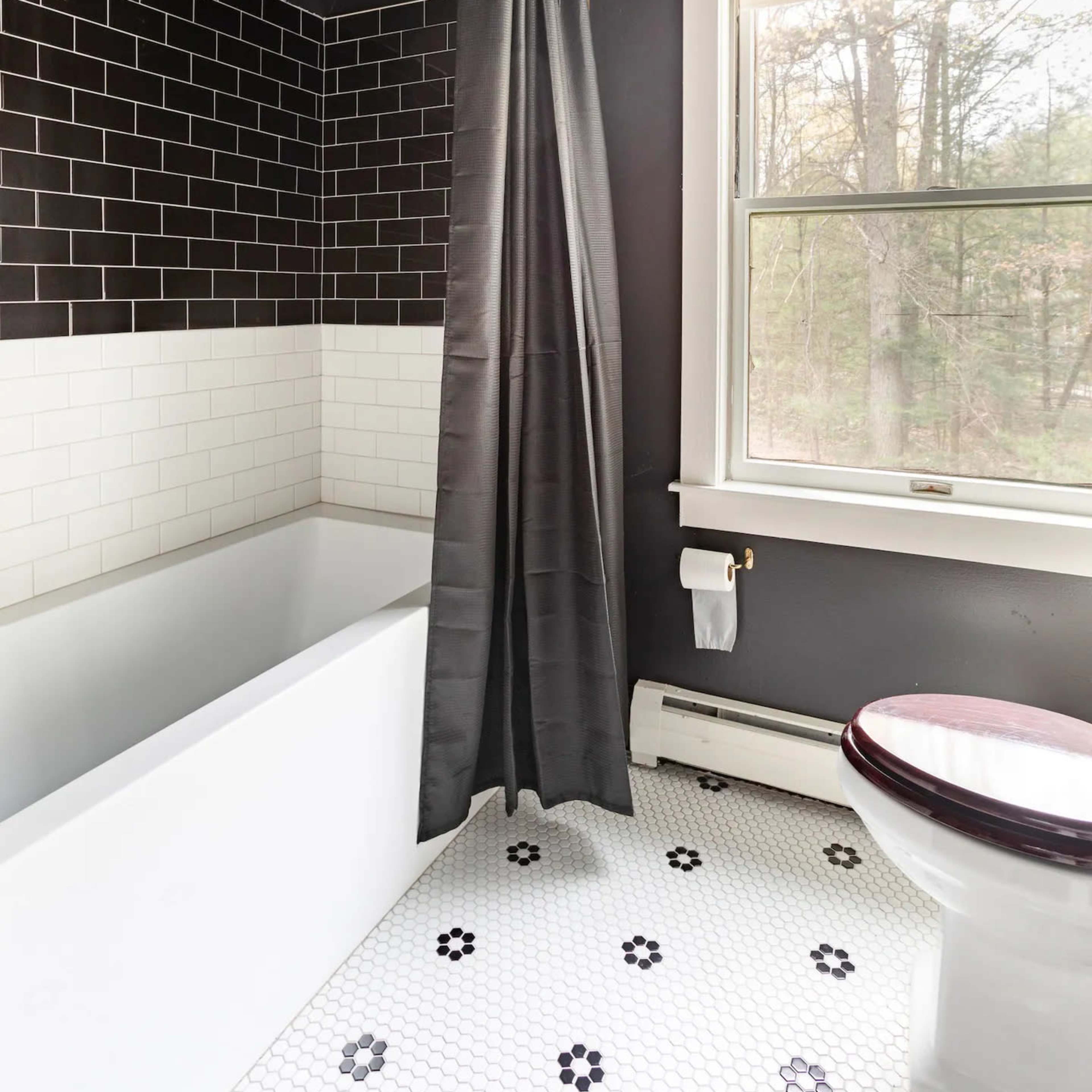 The bathroom features a black and white tile design, a bathtub with a shower curtain, a toilet, and a window with a view.