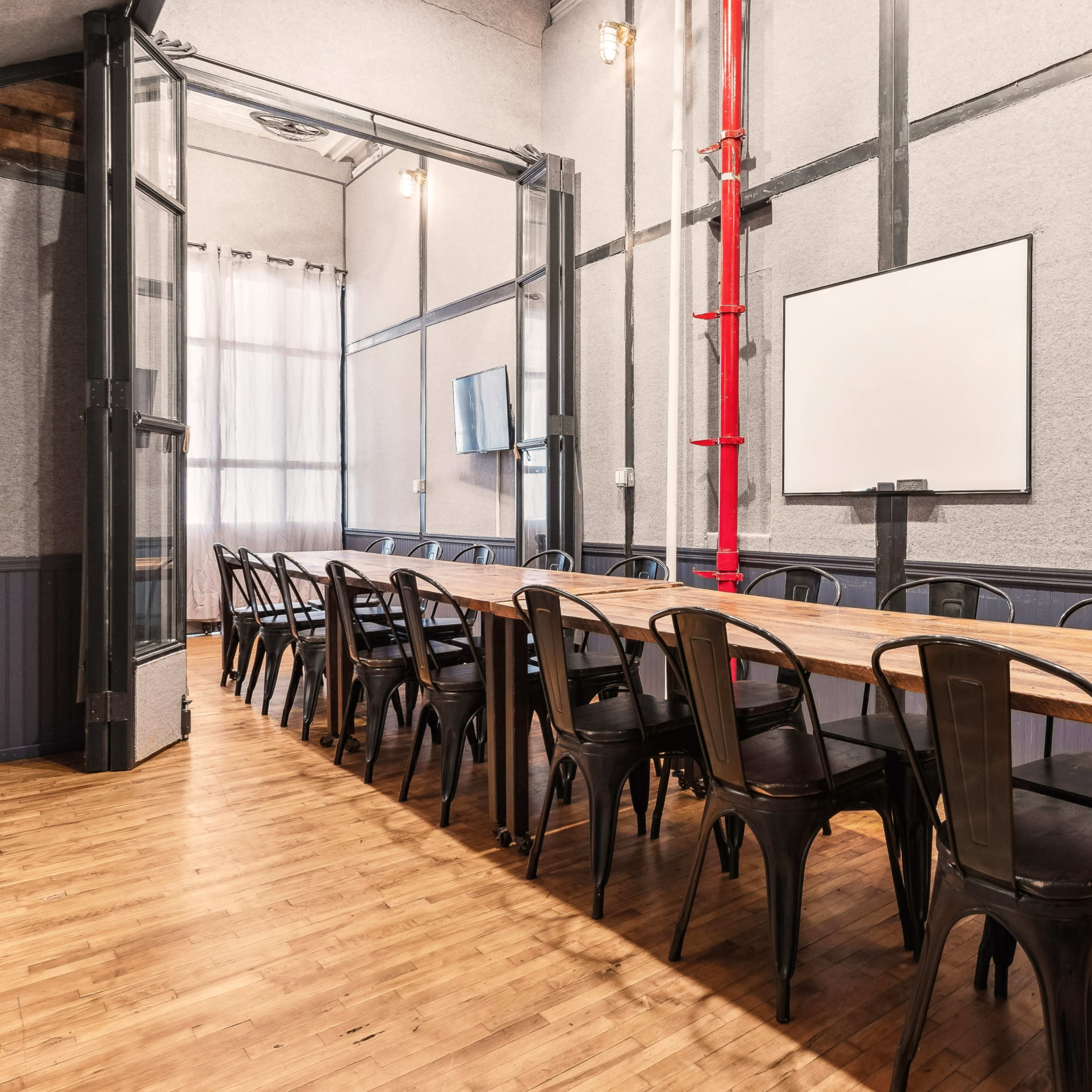 A long wooden table with metal chairs is set up in a conference room featuring two whiteboards and large windows.