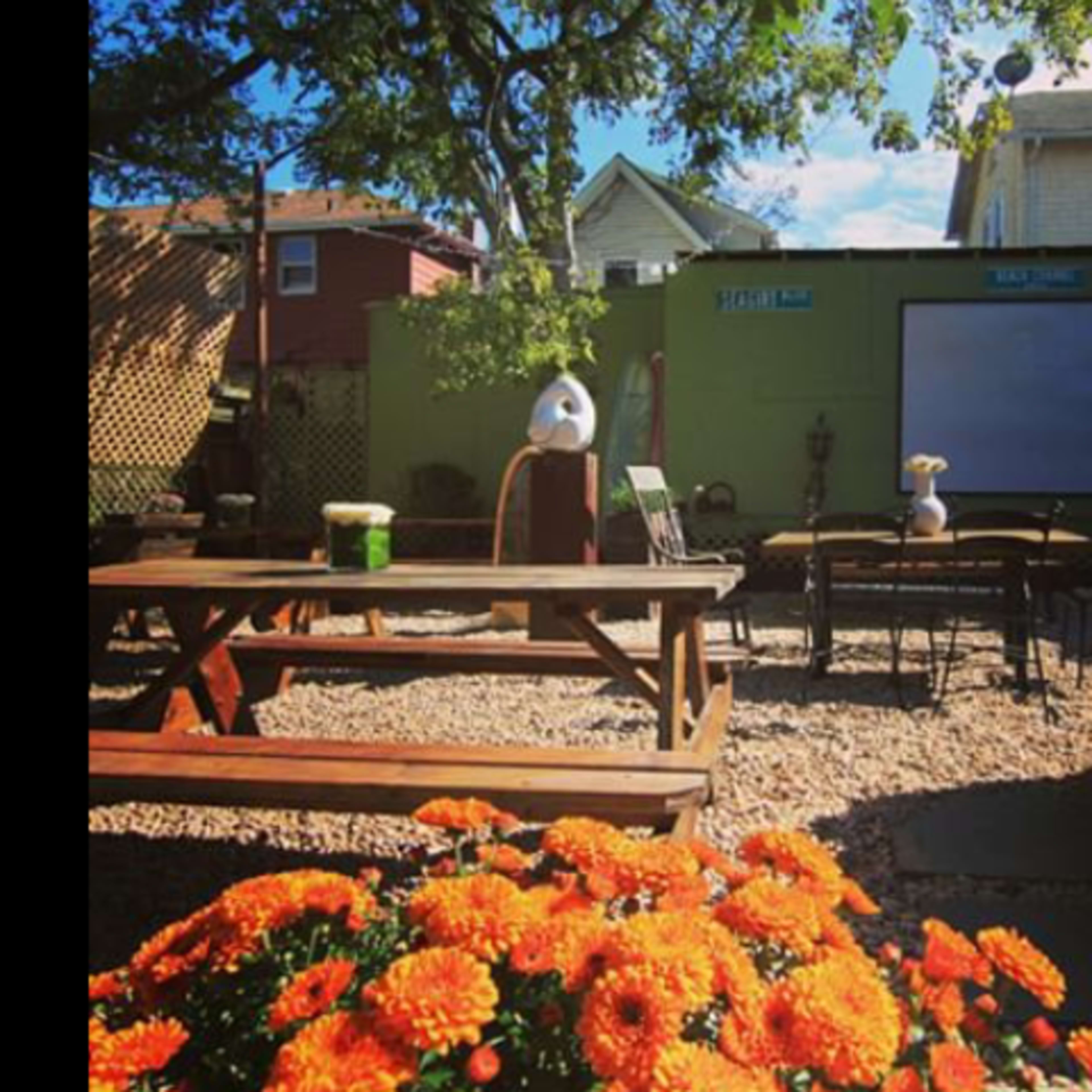 A backyard seating area with a wooden picnic table, several chairs, and vibrant orange flowers in the foreground.