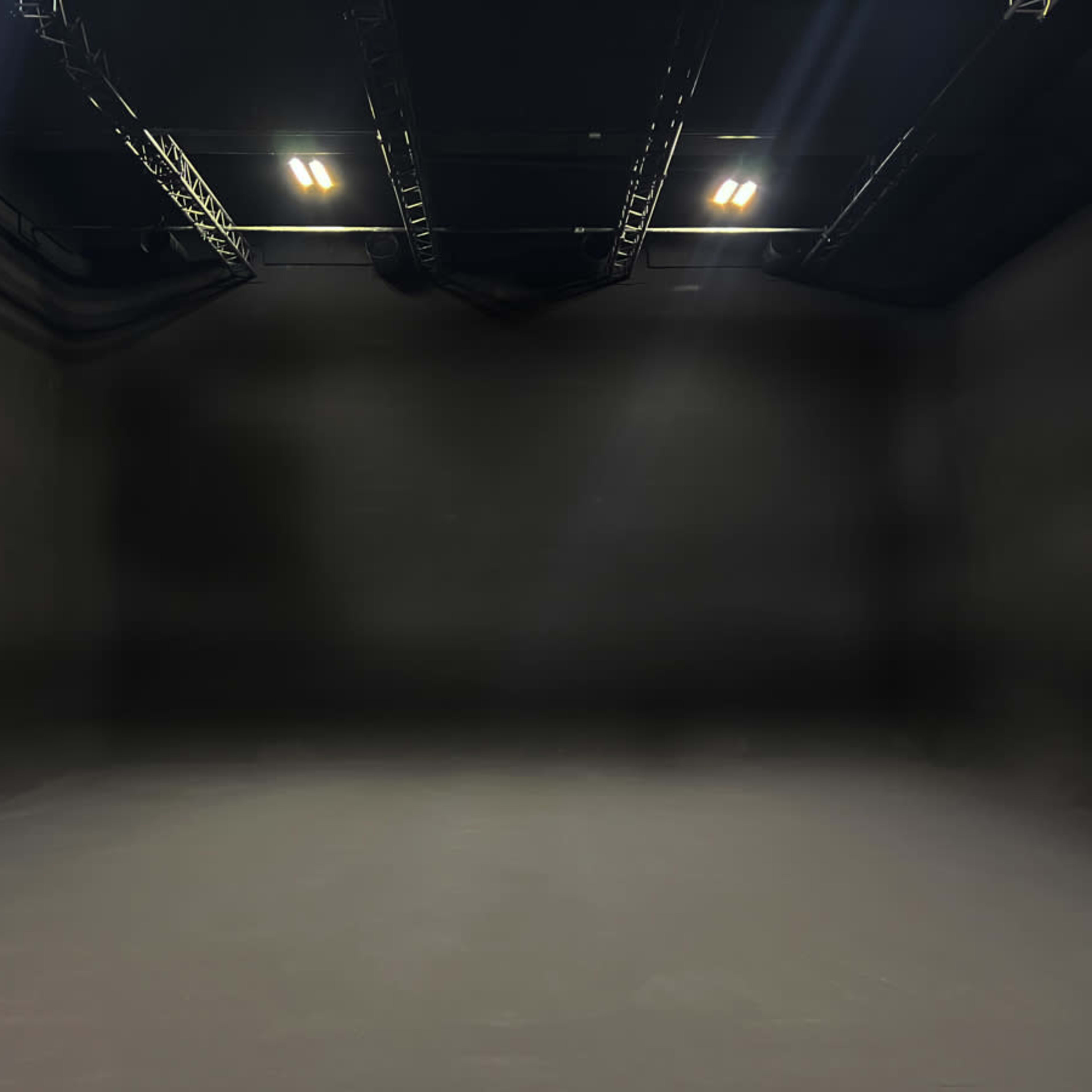 An empty black studio space with overhead lights and a seamless backdrop.