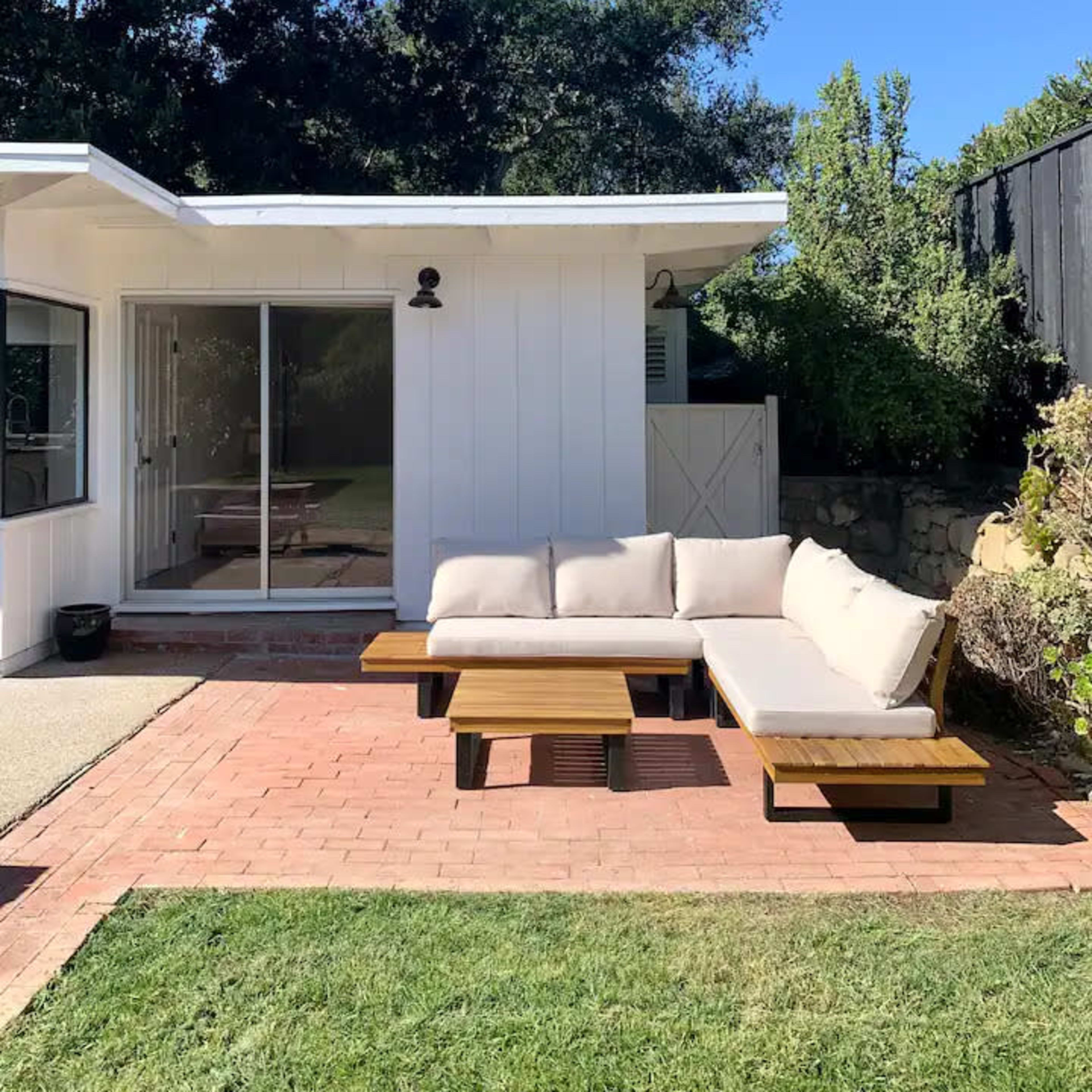 A modern outdoor seating area features a sectional sofa on a brick patio adjacent to a house with a large glass sliding door.