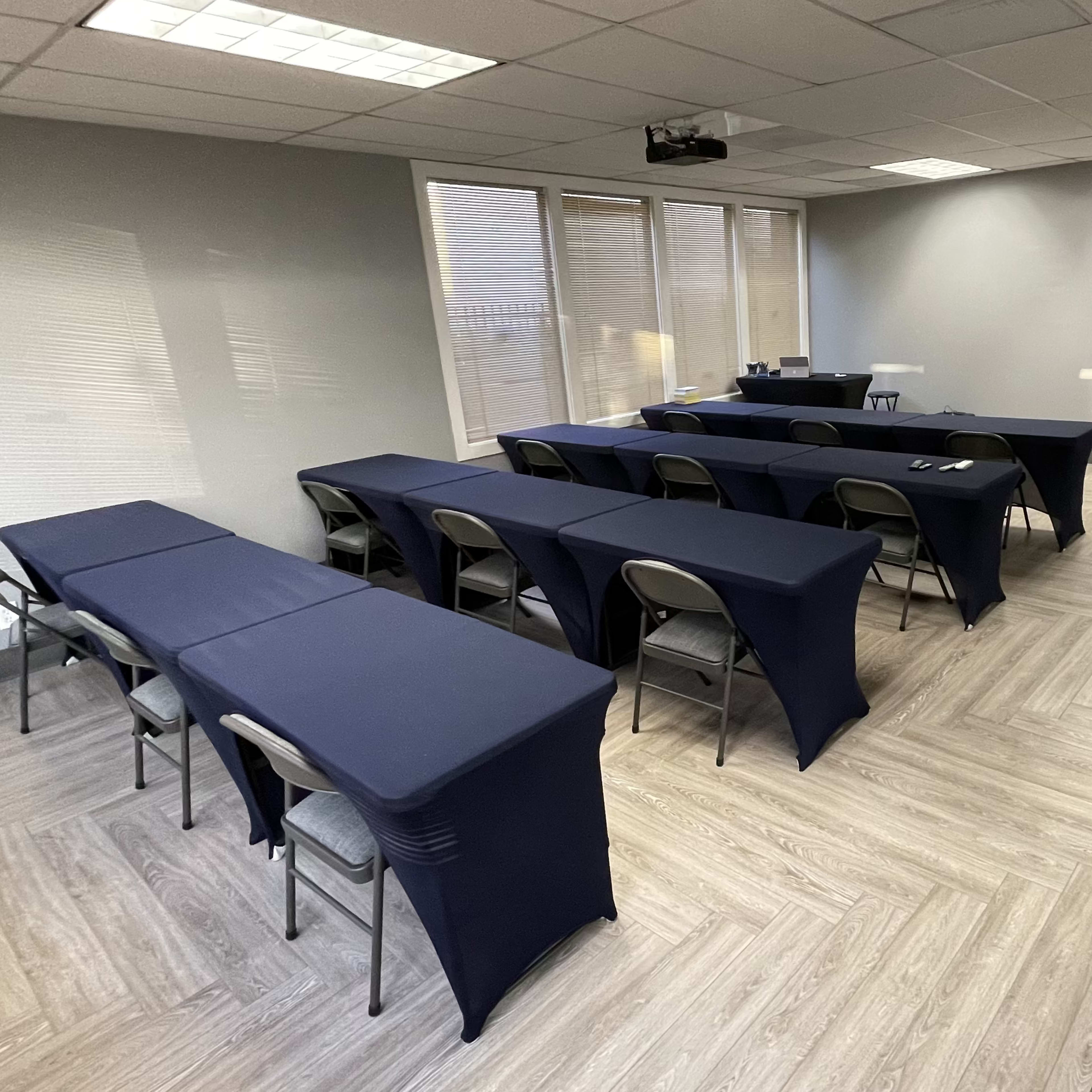 A conference room with two rows of tables covered in navy blue cloth, facing a screen at the front of the room.