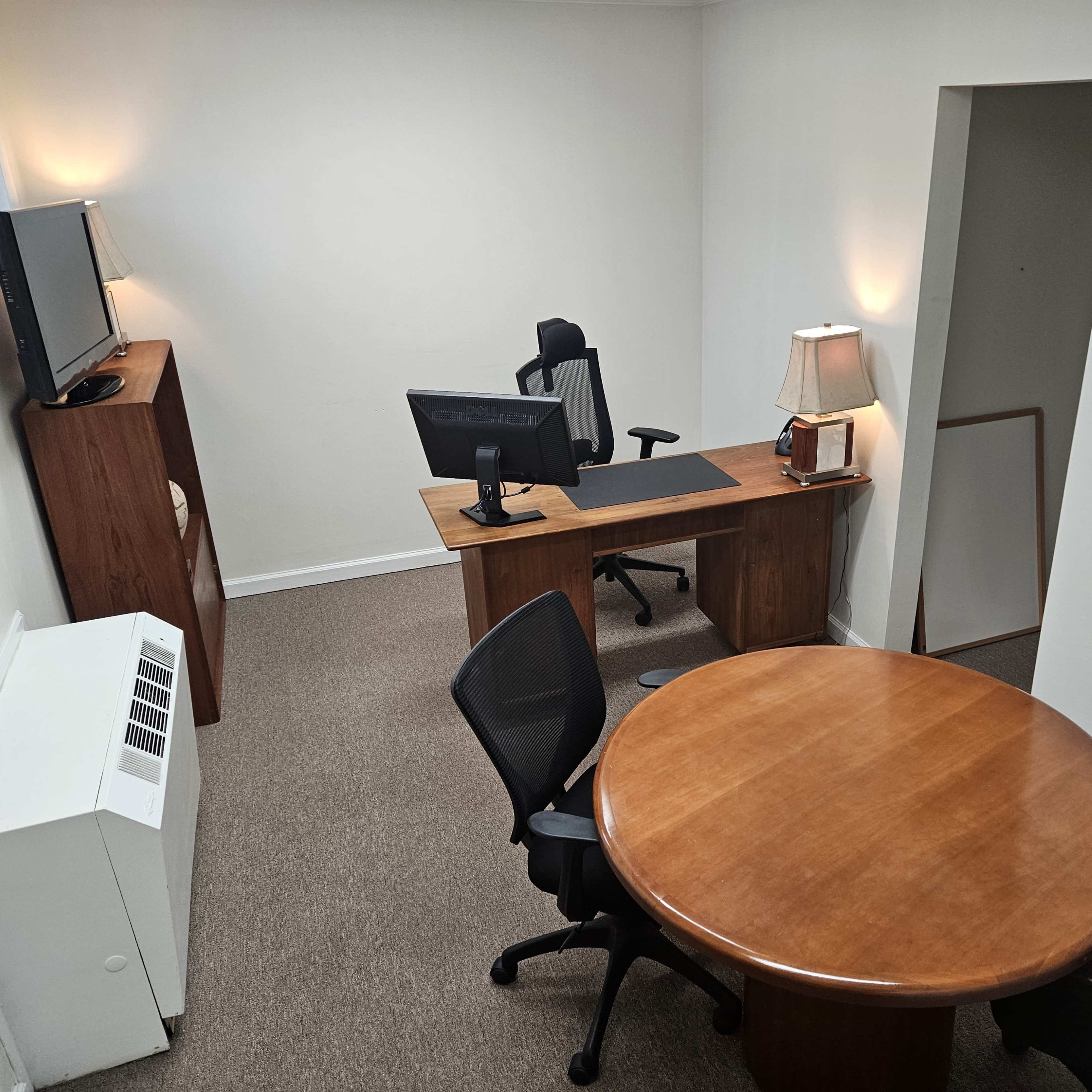 A small office space with a desk, a round table, and a television on a stand.