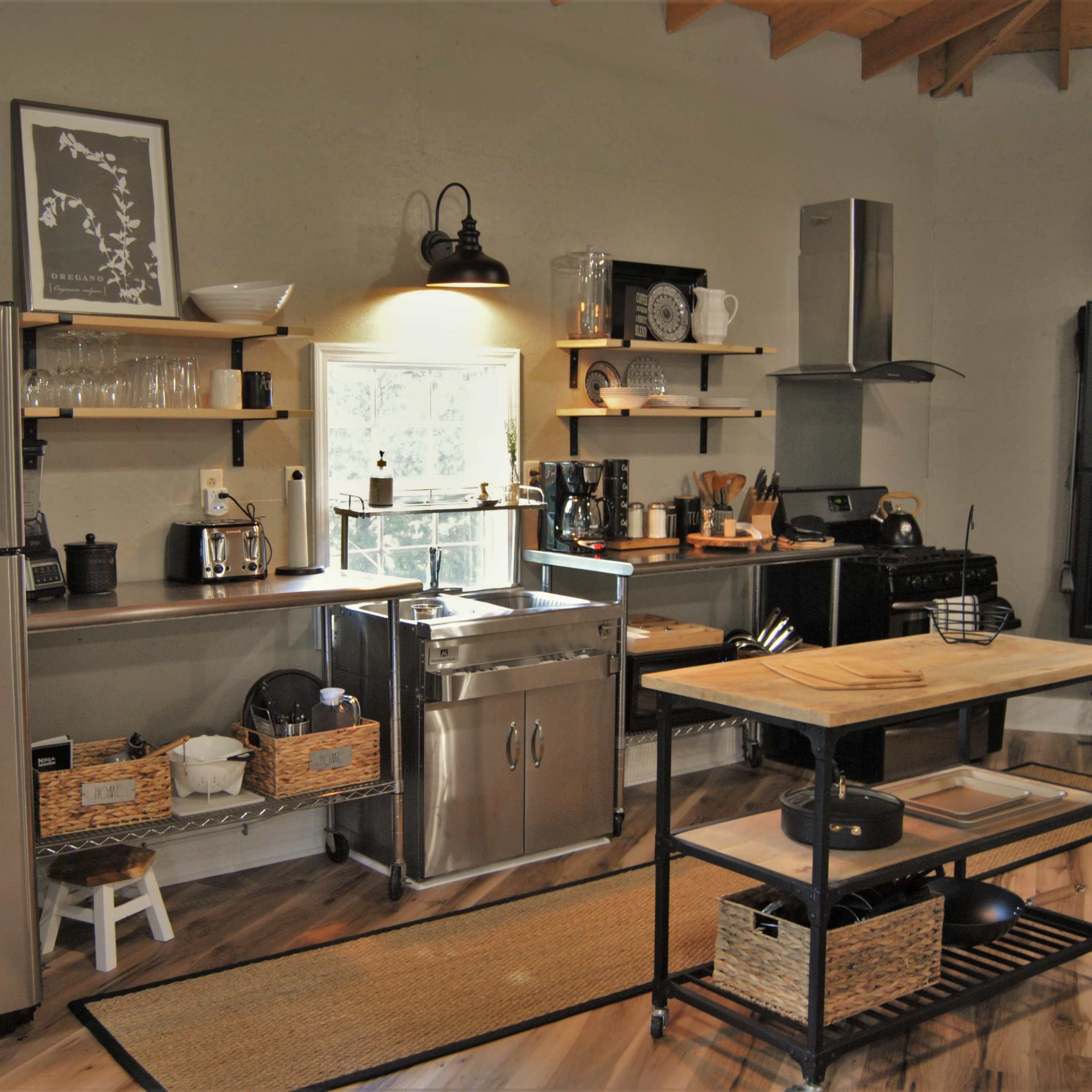A modern kitchen featuring stainless steel appliances, wooden shelves with kitchenware, and a central island with a metal frame.