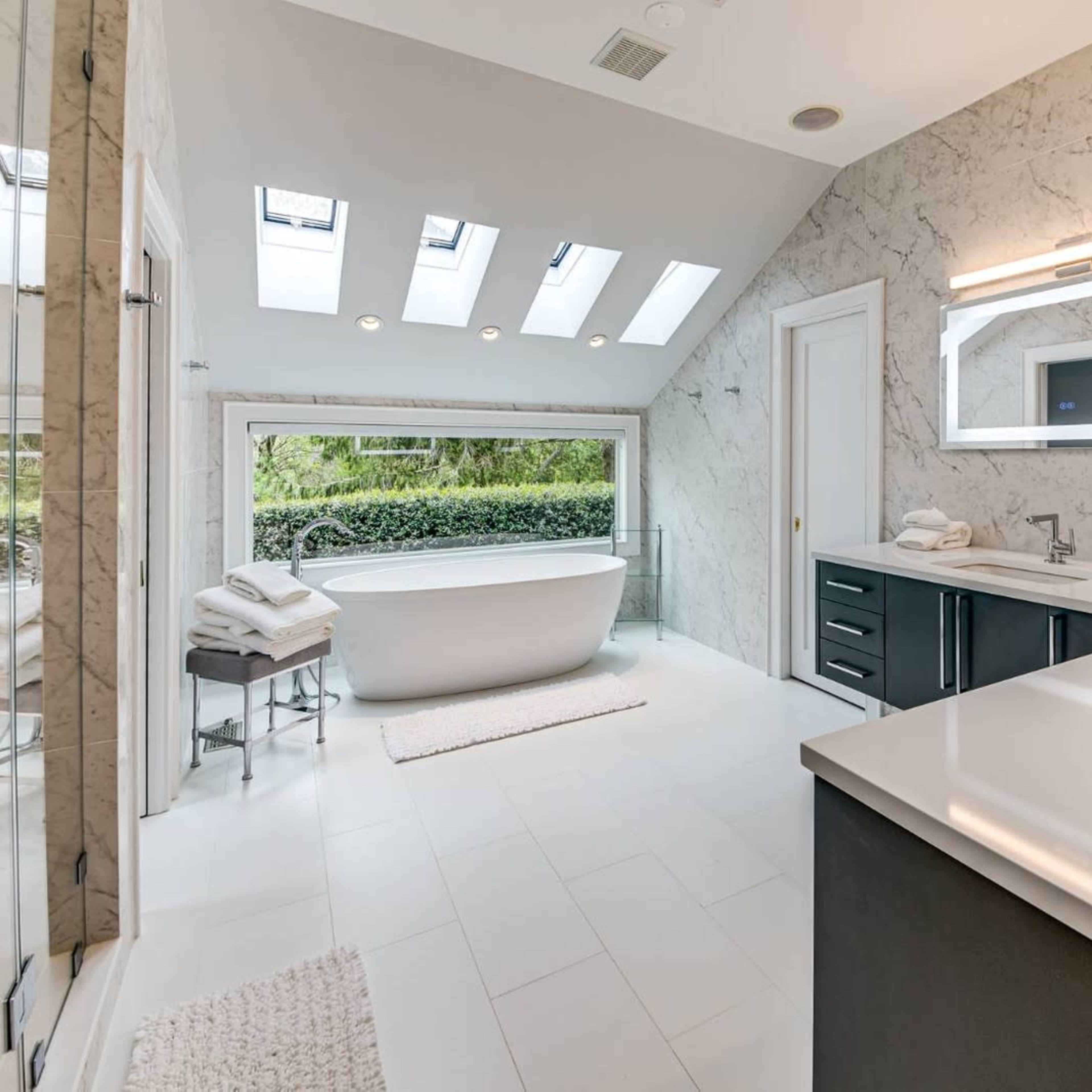 A modern bathroom featuring a freestanding bathtub, a large mirror, and skylights that provide natural light.