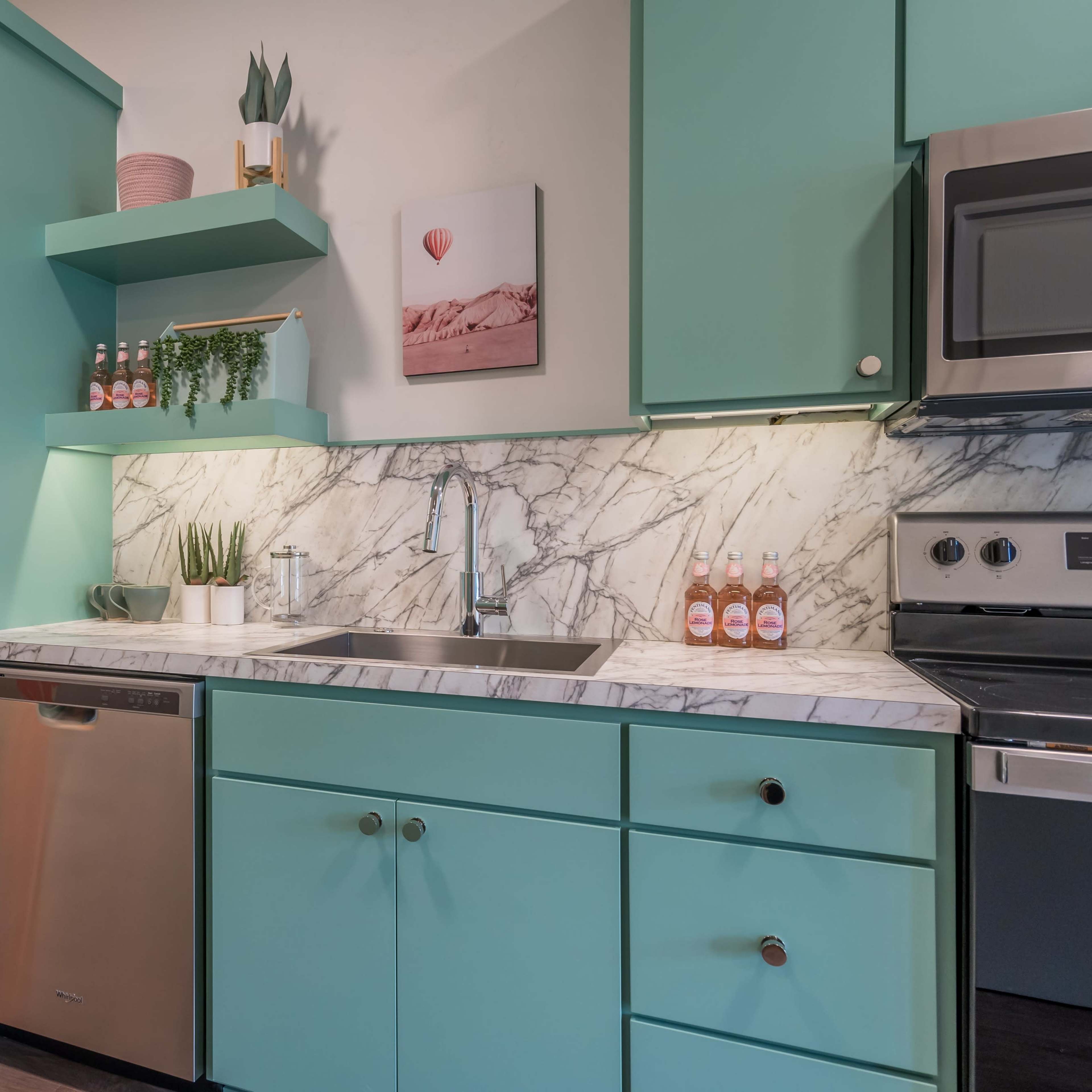 A modern kitchen featuring mint-green cabinets, a stainless steel refrigerator, and a marble countertop with a sink and stainless steel dishwasher.