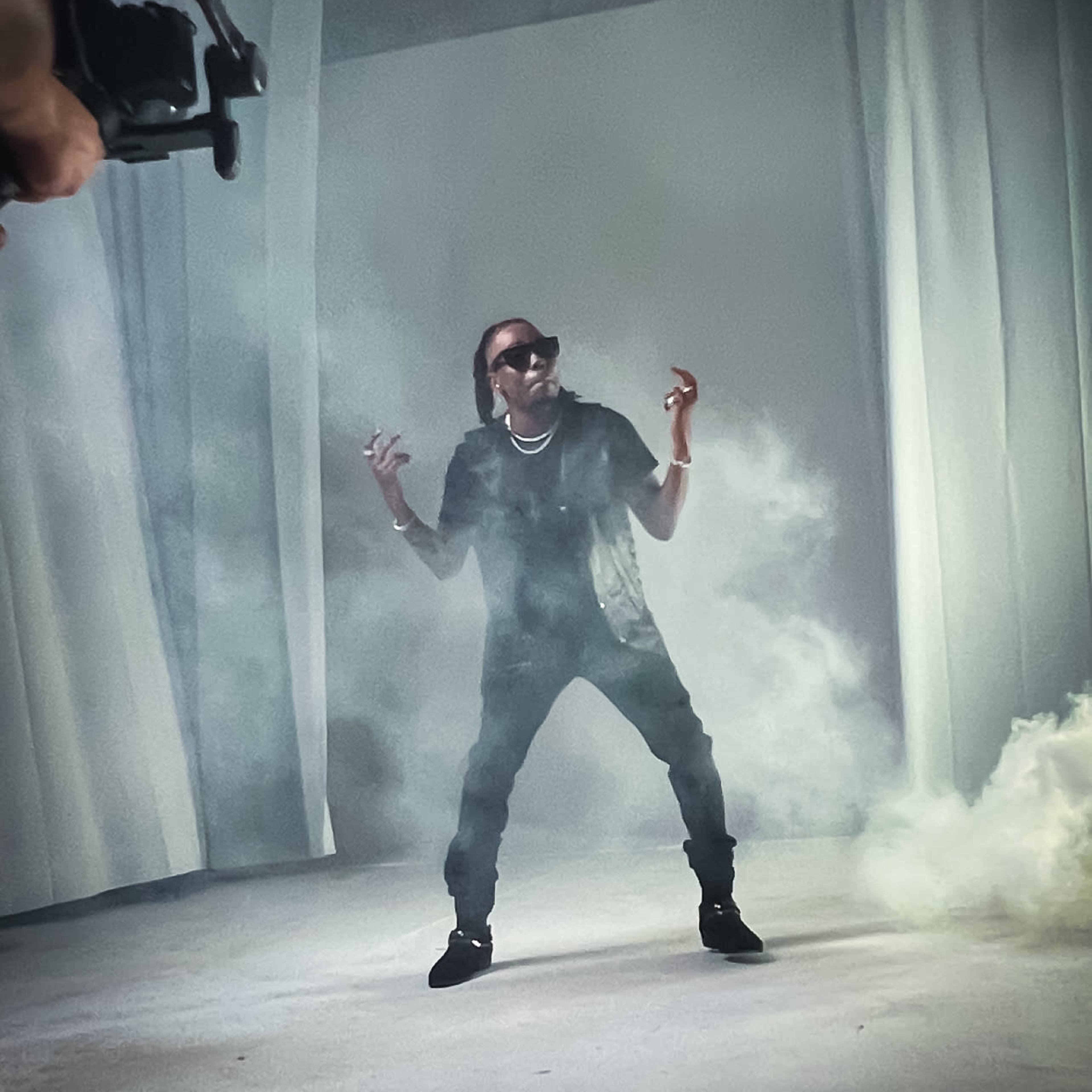 A person stands in a smoky room, striking a pose while being filmed.