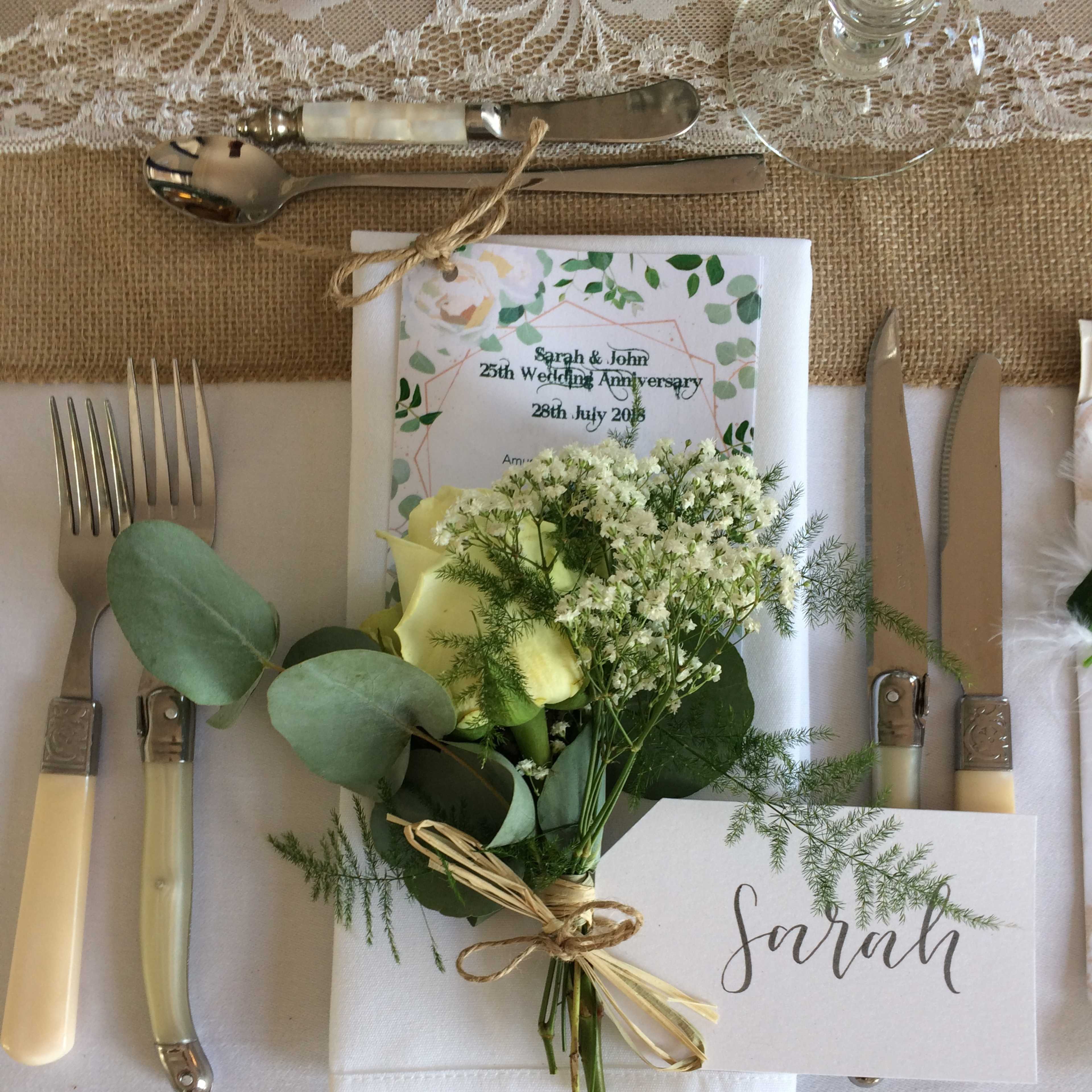 A table setting features a neatly folded napkin, a floral arrangement with greenery, and a name card for "Sarah" beside a menu for a wedding anniversary celebration.