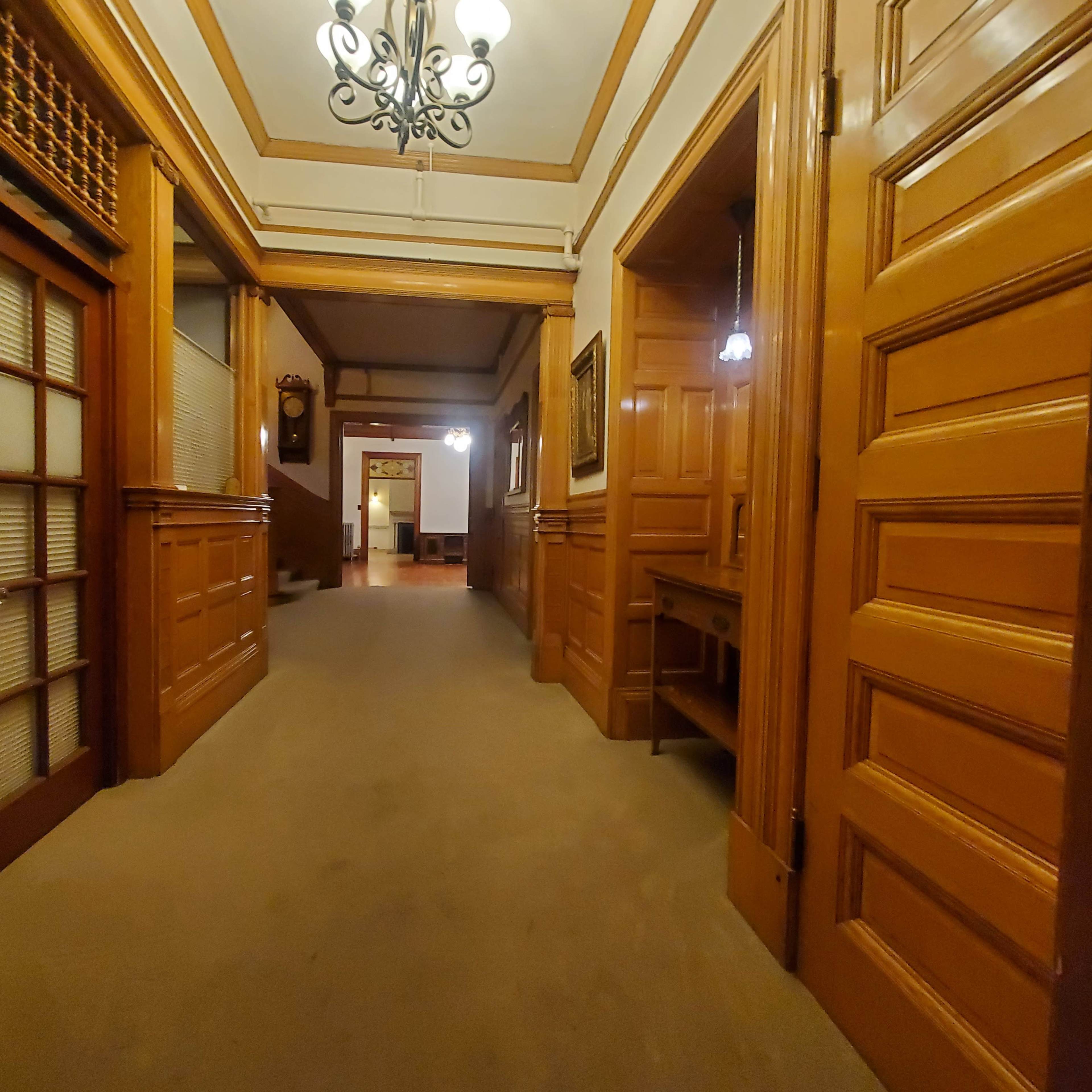 A long hallway features wooden paneling, a chandelier, and several doors along the sides.