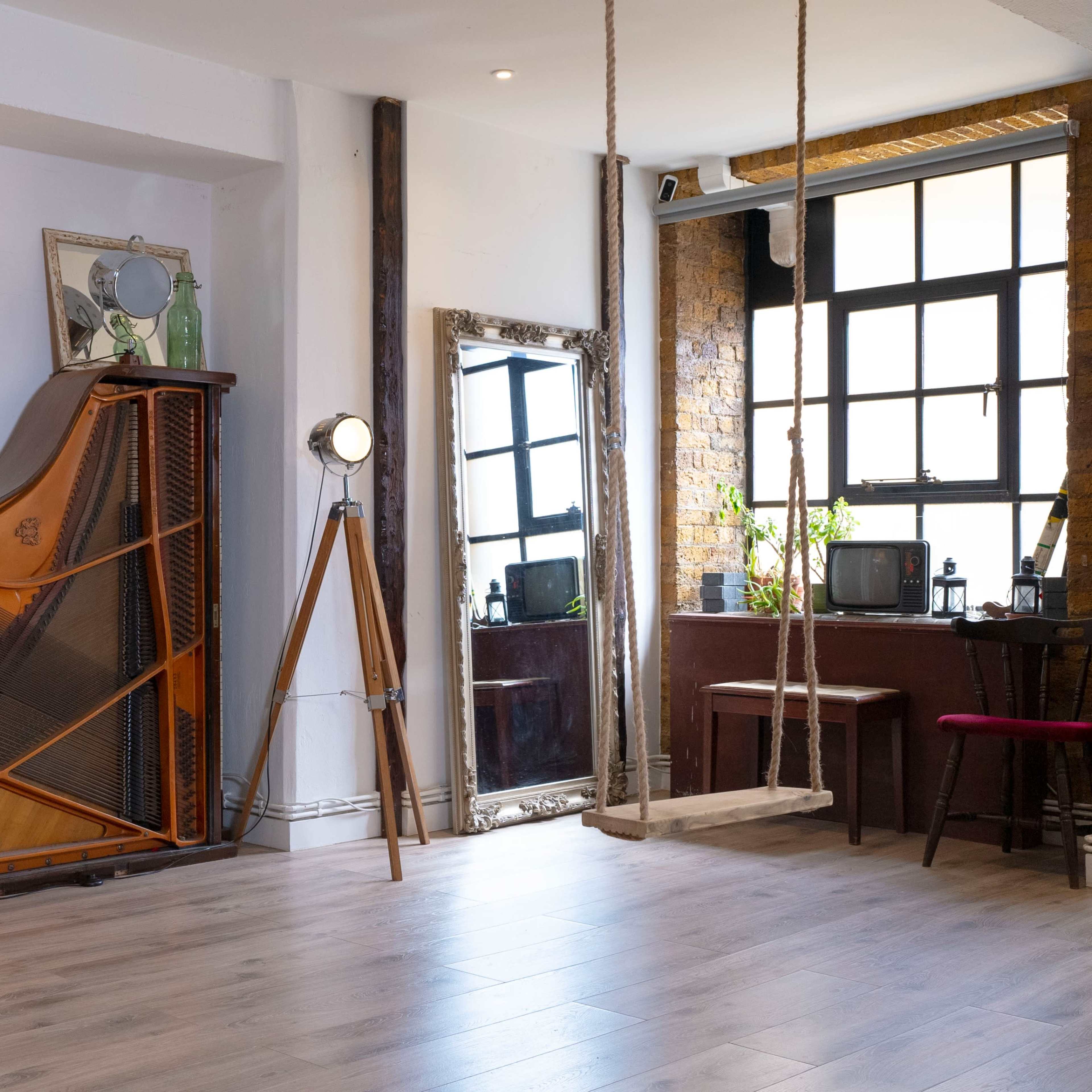 A spacious, well-lit interior features a grand piano against the wall, a floor lamp, a mirror, and a swing, with bookshelves and vintage decor.