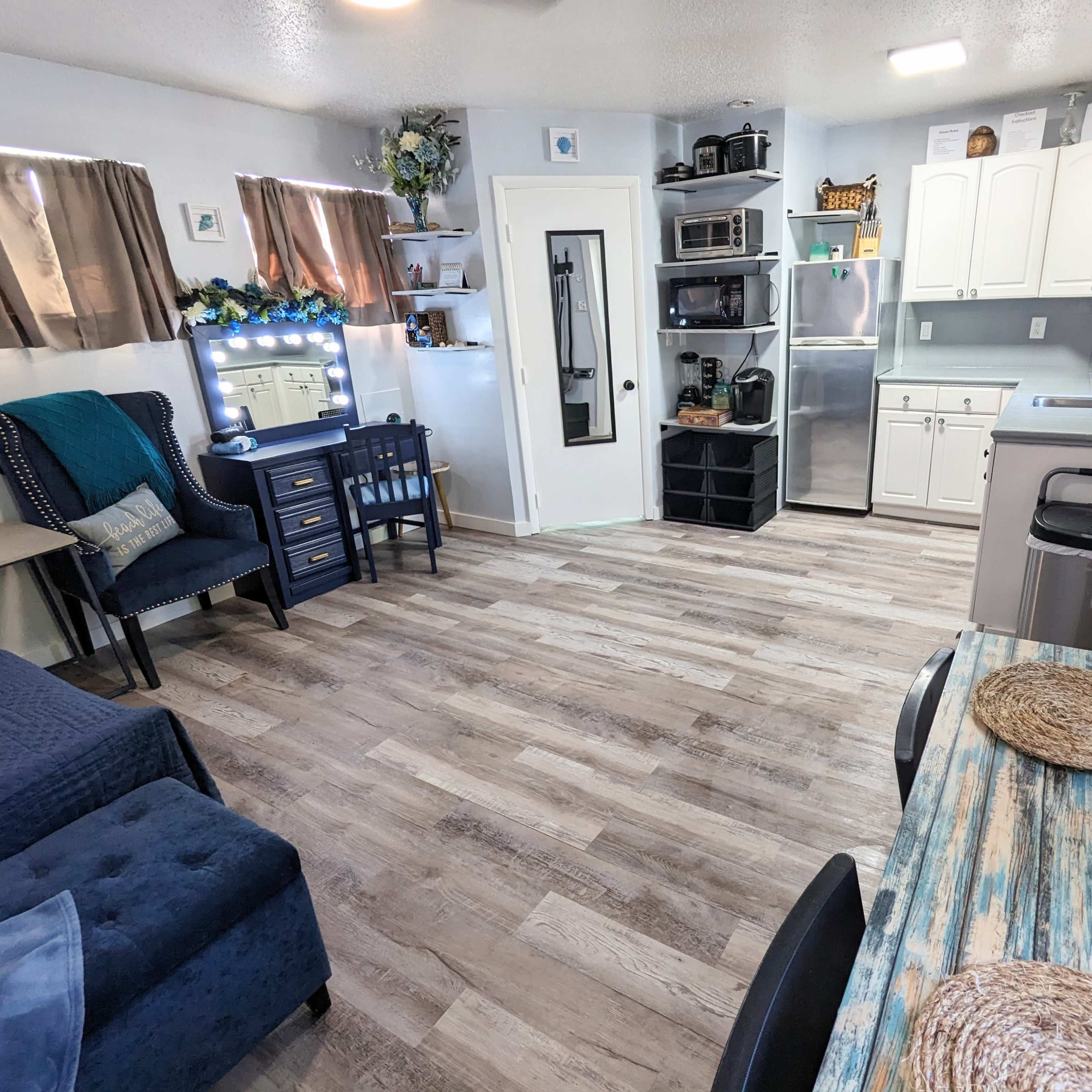 A small, modern kitchen and living area featuring a sofa, a dining table, a desk, and various appliances.