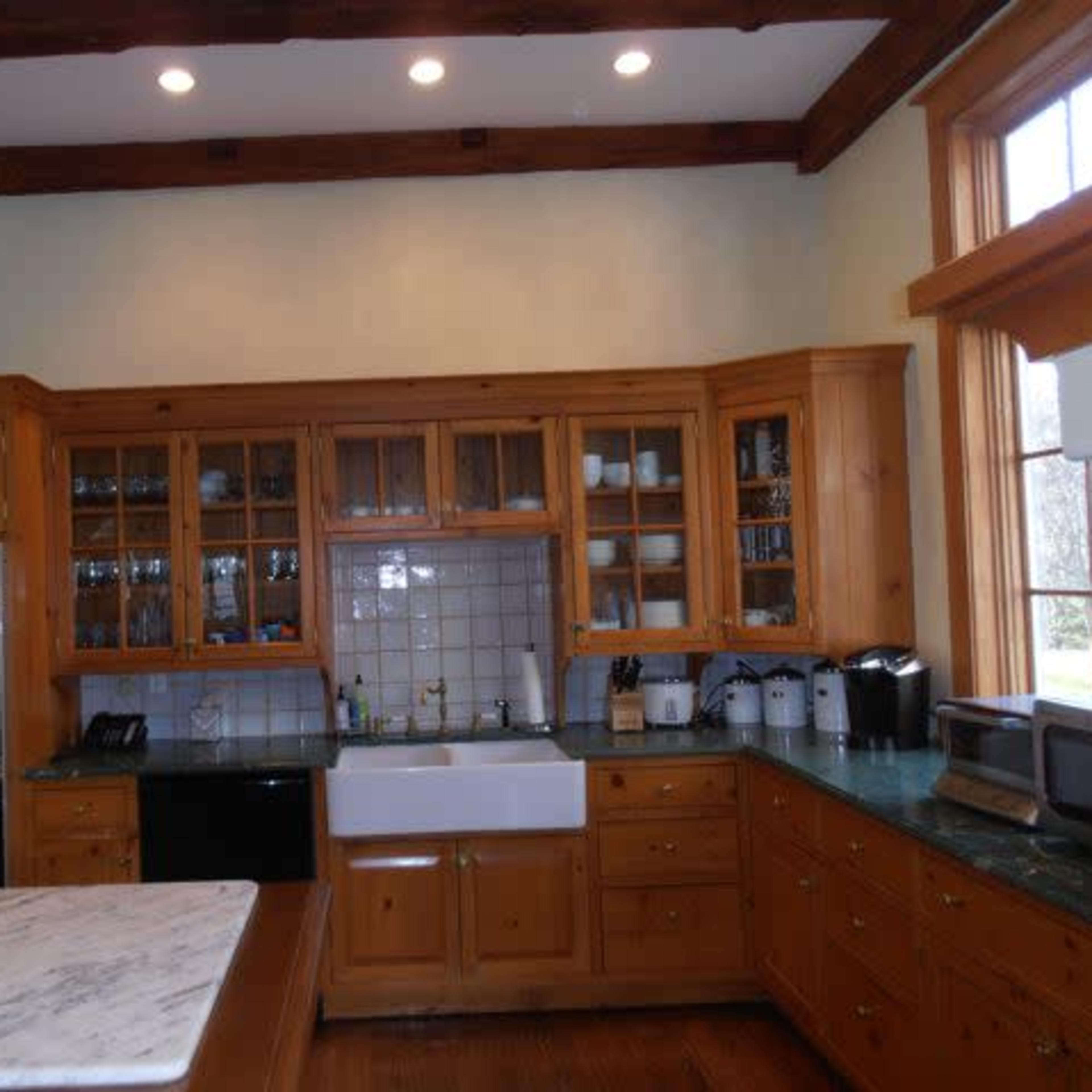 A wooden kitchen features a large farmhouse sink, glass-front cabinets, and multiple appliances.