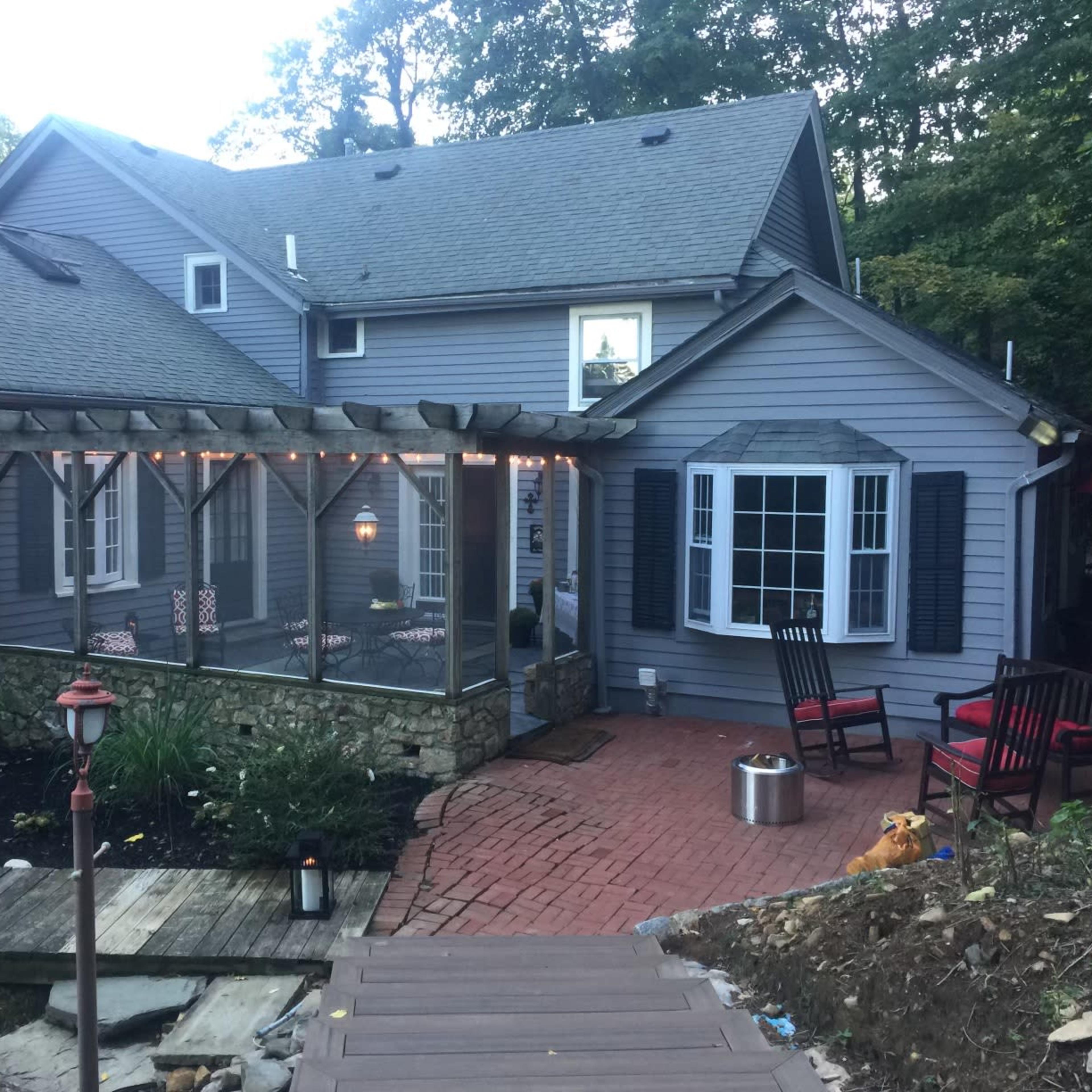 A gray house with a screened-in porch, surrounded by trees, a brick patio, and outdoor seating.