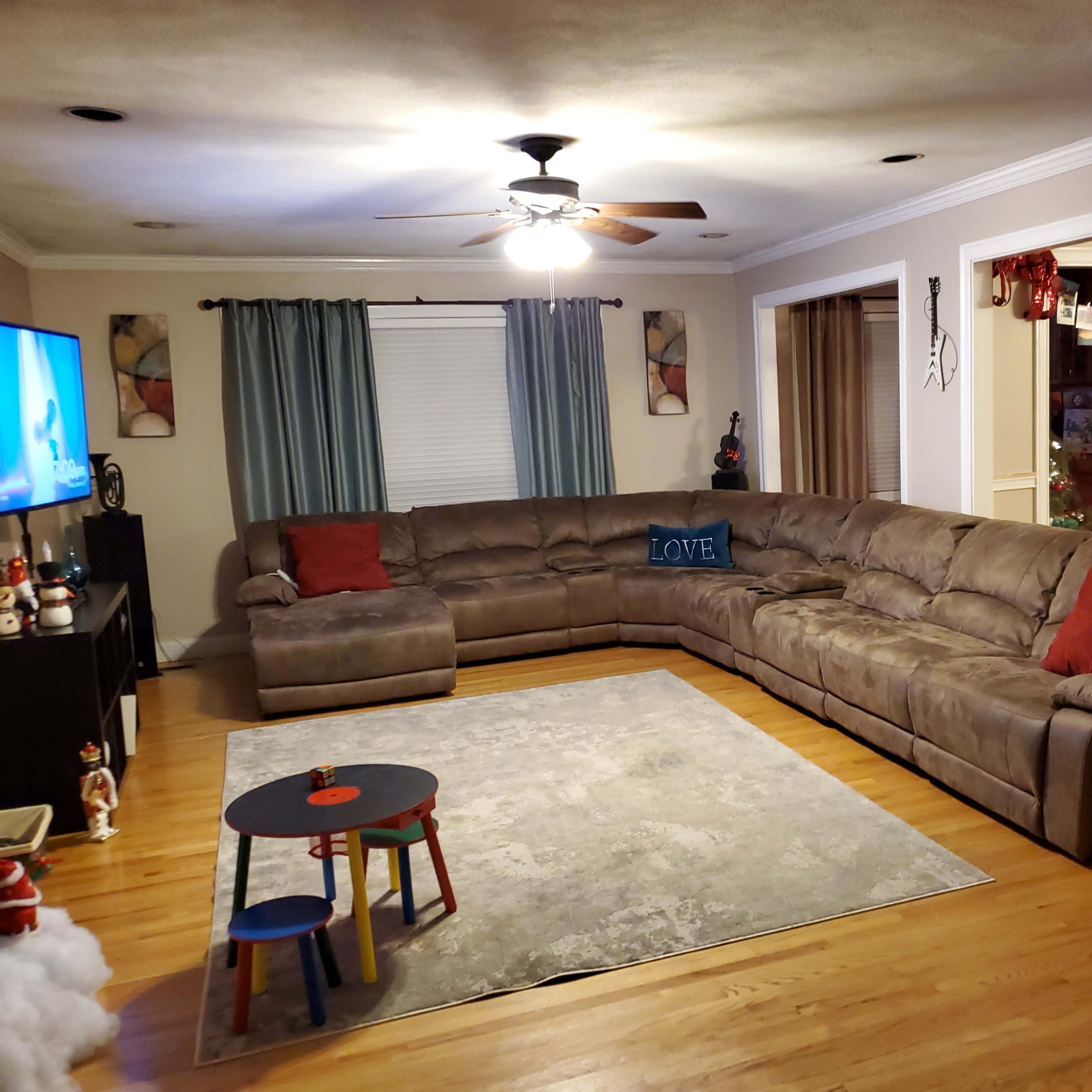 A spacious living room features a large sectional sofa, a low coffee table, and a television set against the wall.