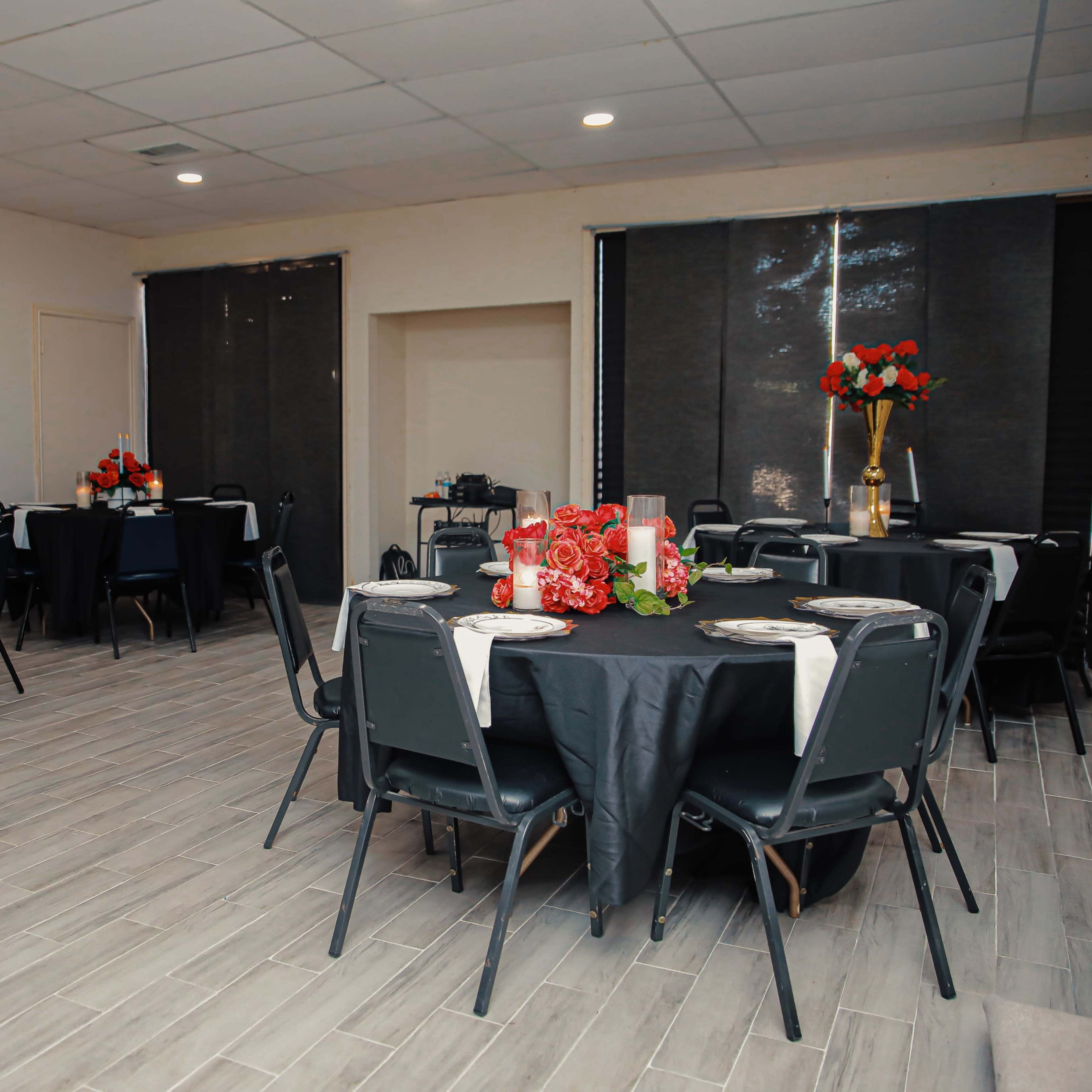 A banquet room with several round tables set with black tablecloths, plates, and floral centerpieces.