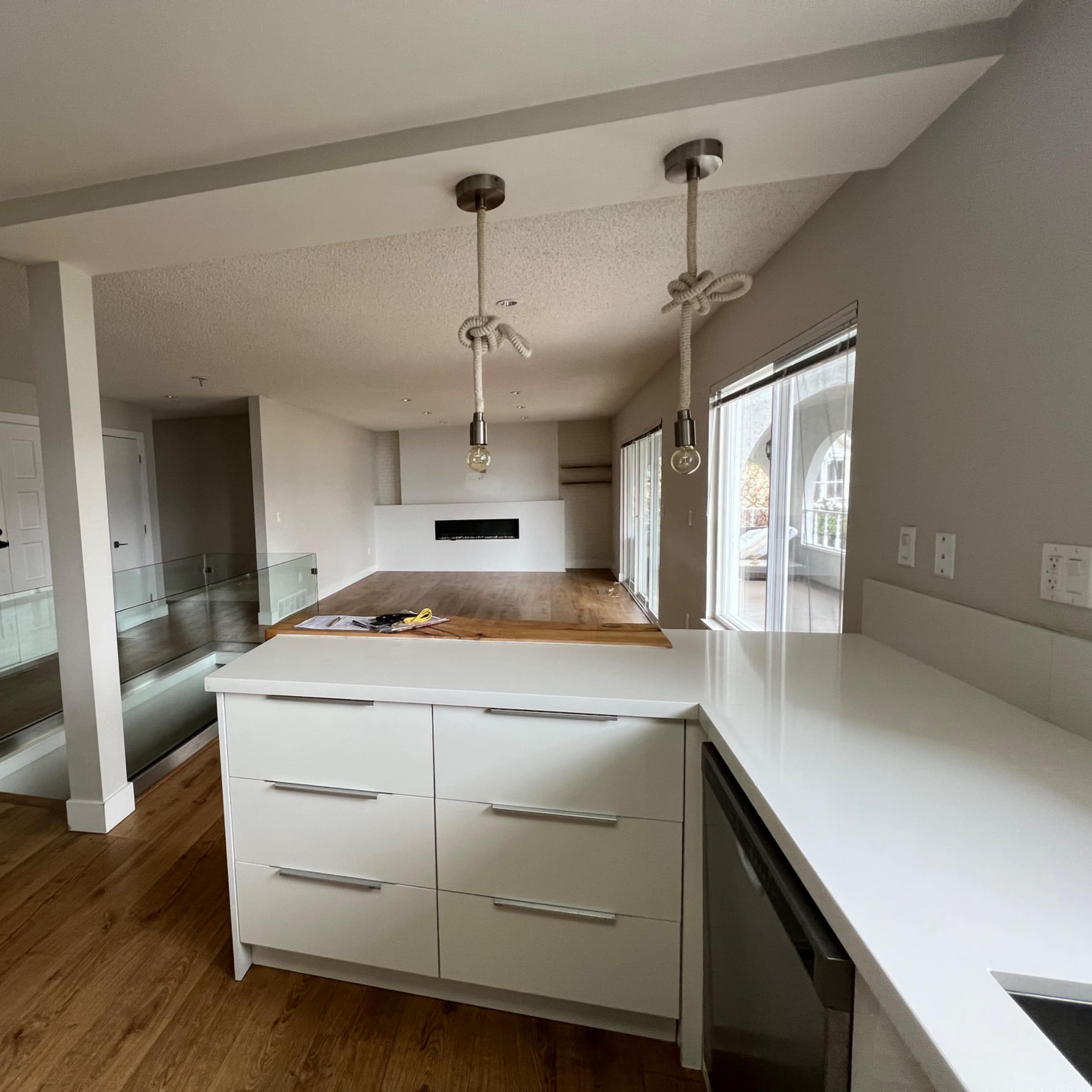 A modern kitchen with a central island, white cabinetry, and an open layout leading to a living area with large windows.