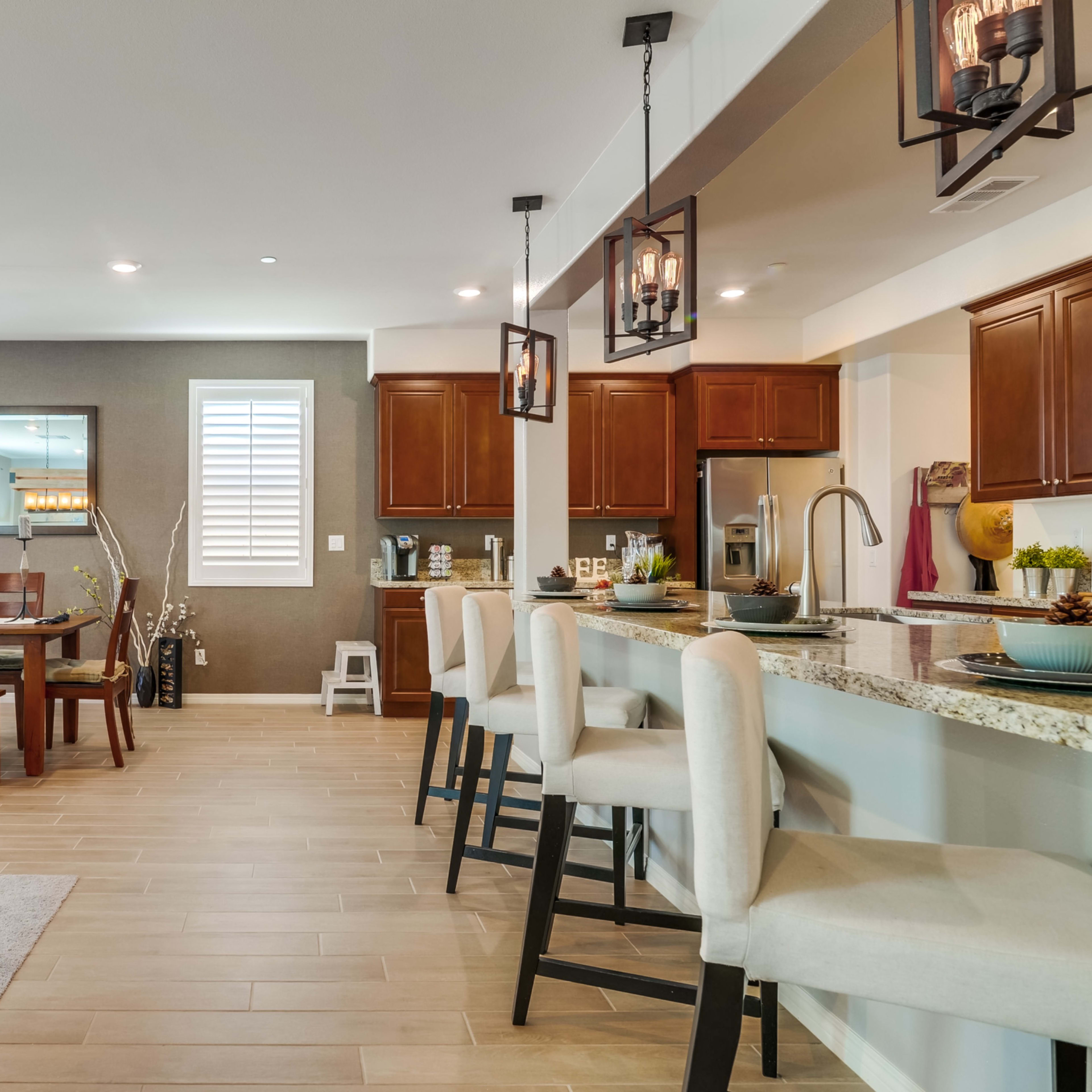 A modern open-concept kitchen and dining area featuring wooden cabinetry, a large dining table, and stylish bar stools.