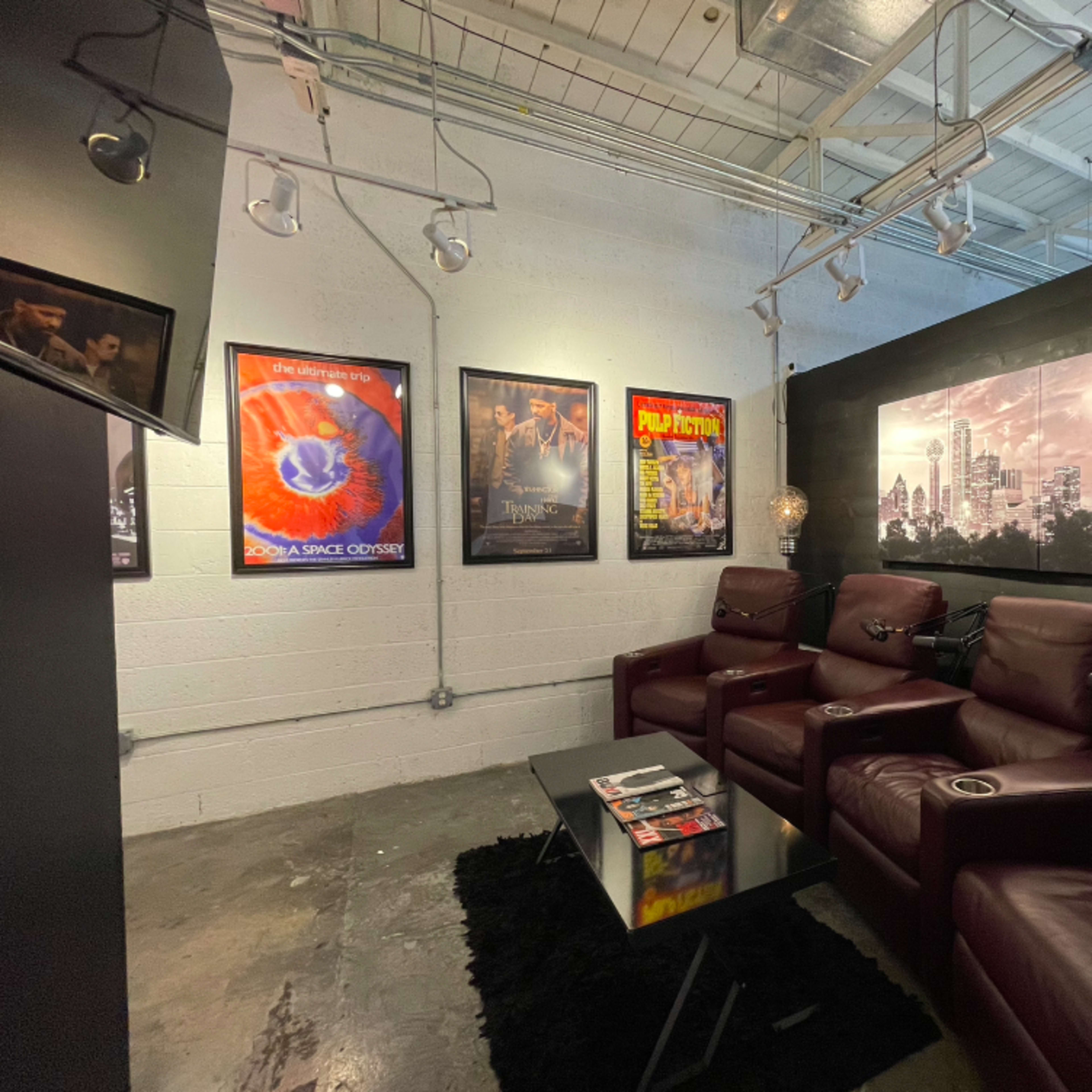 A home theater room featuring dark leather recliners arranged in front of a coffee table, with various movie posters displayed on the walls.