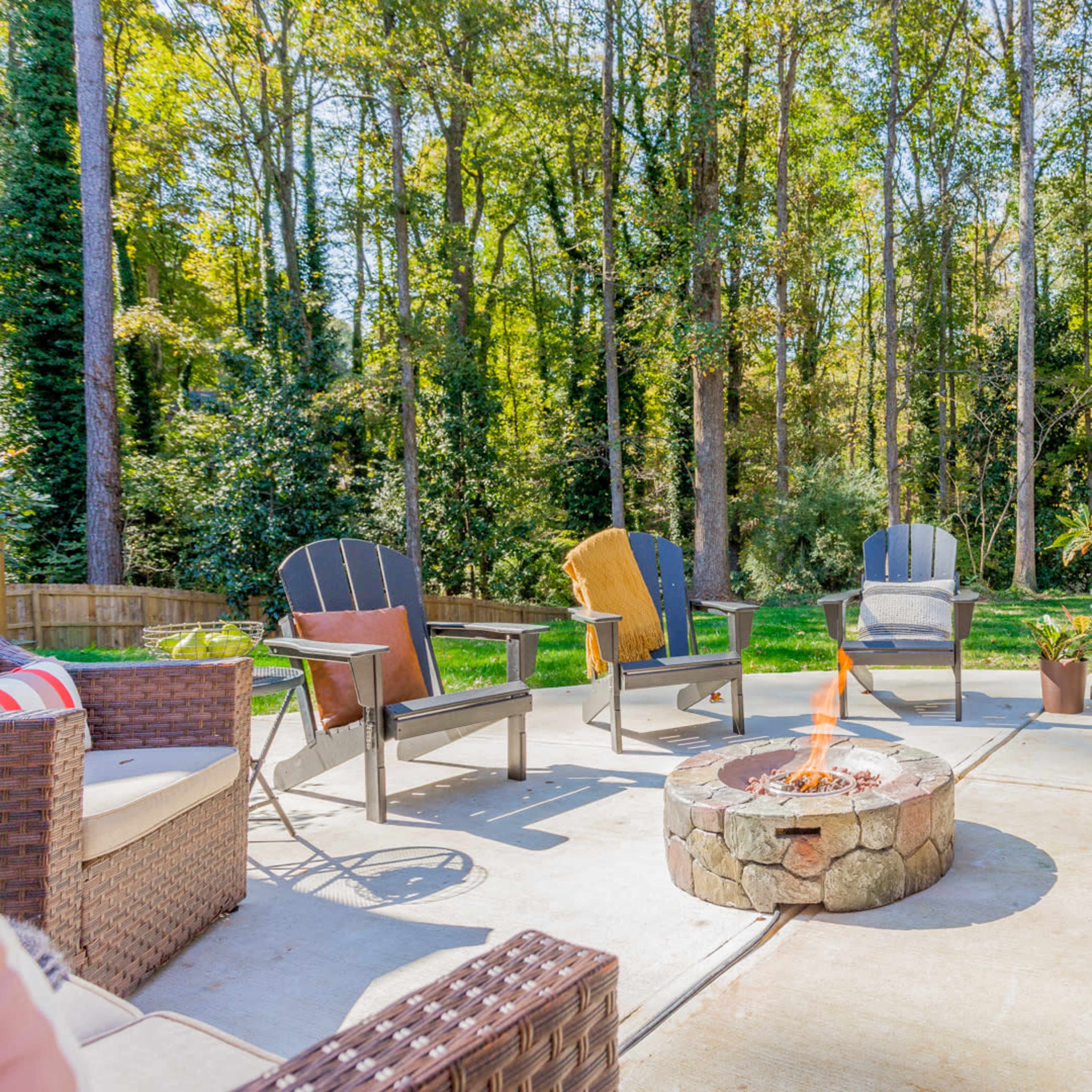 A stone fire pit surrounded by several outdoor chairs on a patio, with trees in the background.