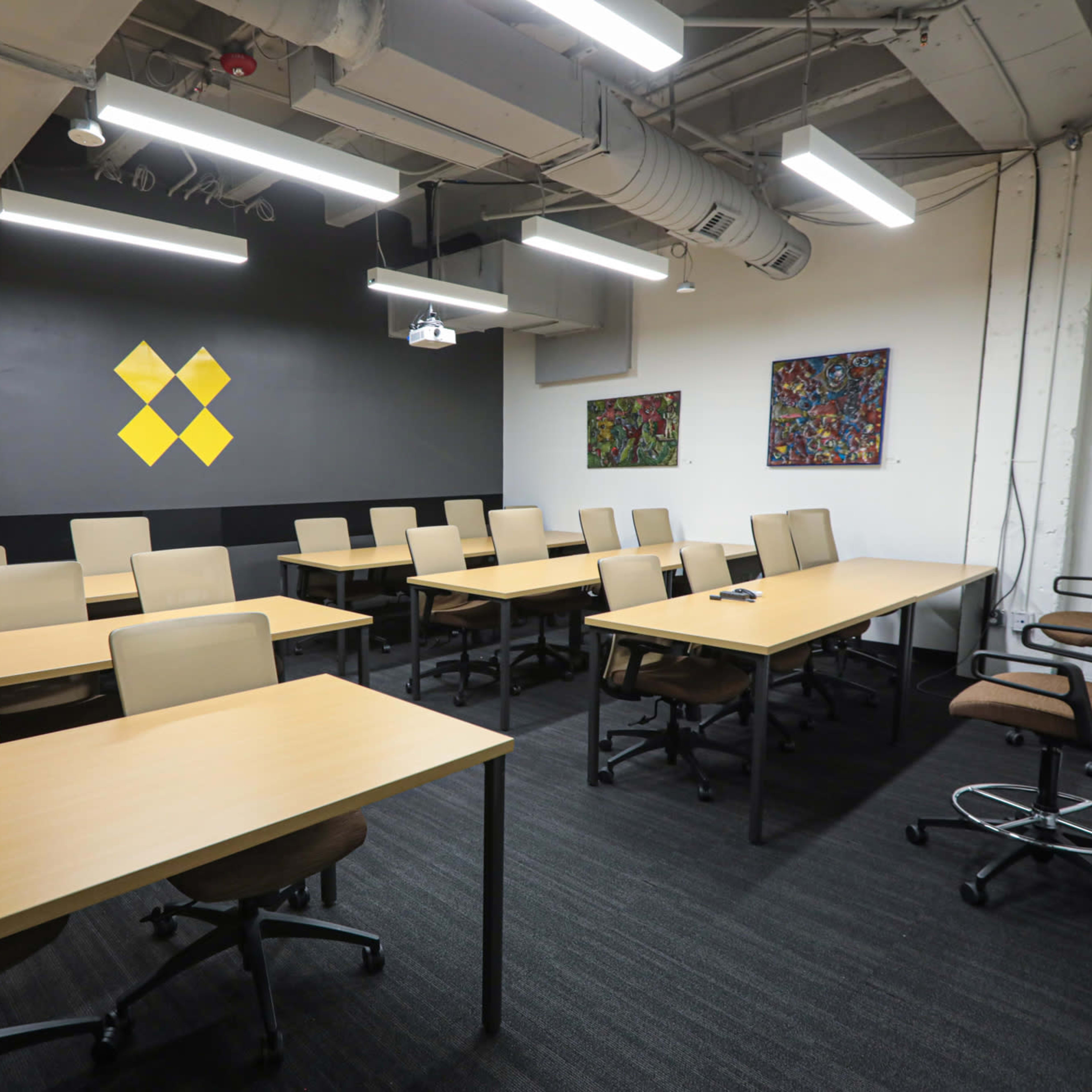 A modern meeting room with multiple rows of tables and chairs, and two artworks displayed on the wall.