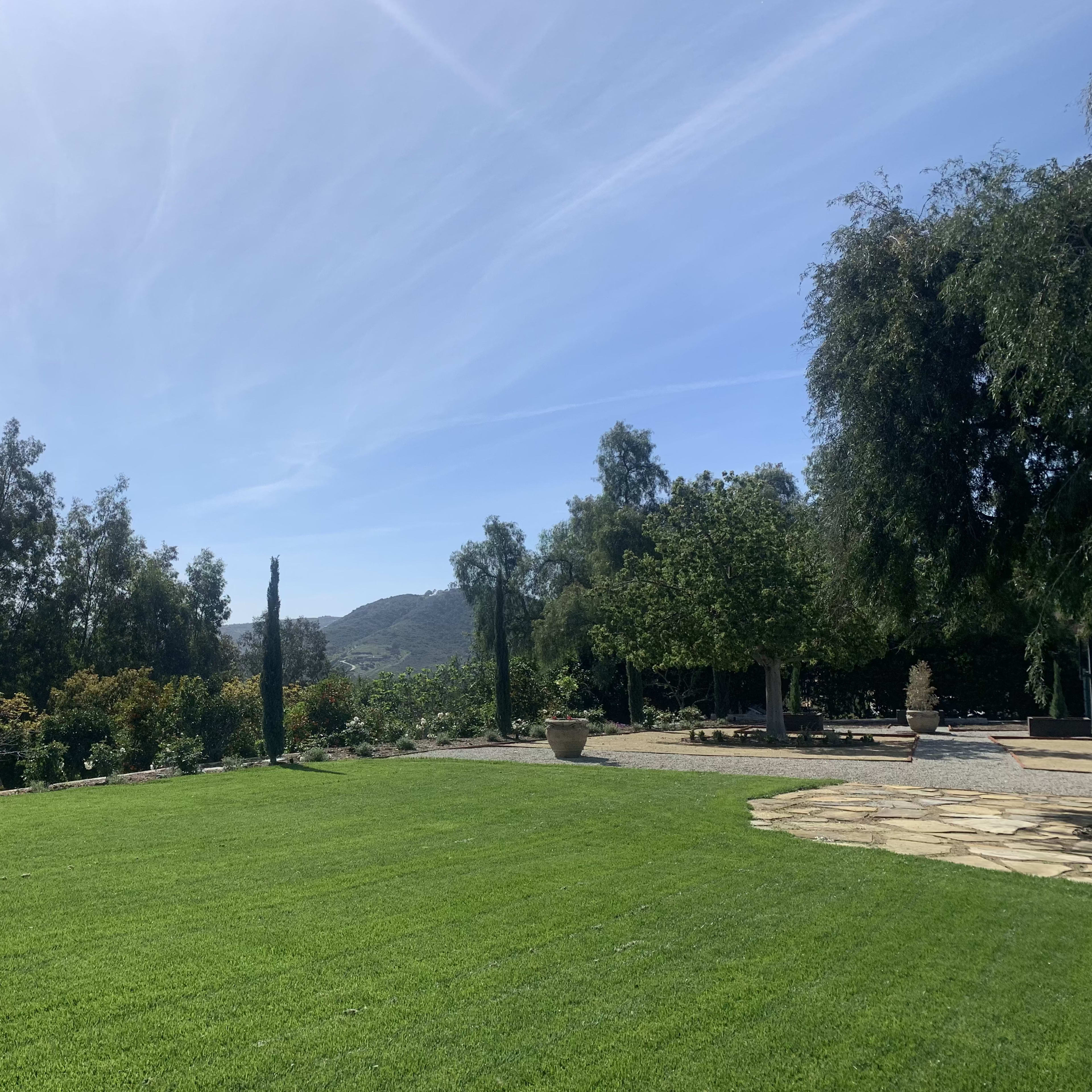 A spacious green lawn bordered by trees, with distant hills and a clear blue sky in the background.