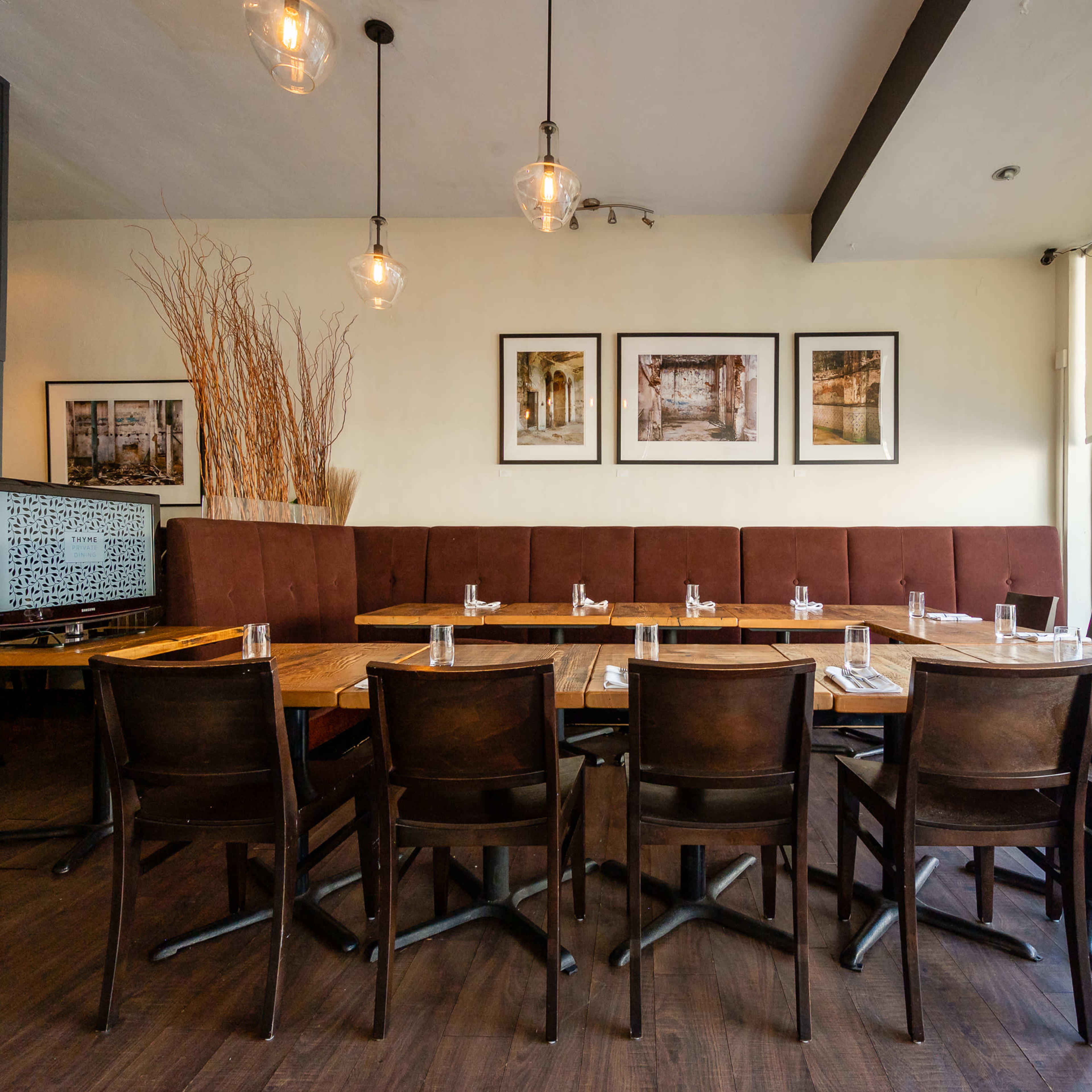 A modern restaurant interior with a long table set for dining, surrounded by dark wooden chairs and decor featuring framed pictures on the wall.
