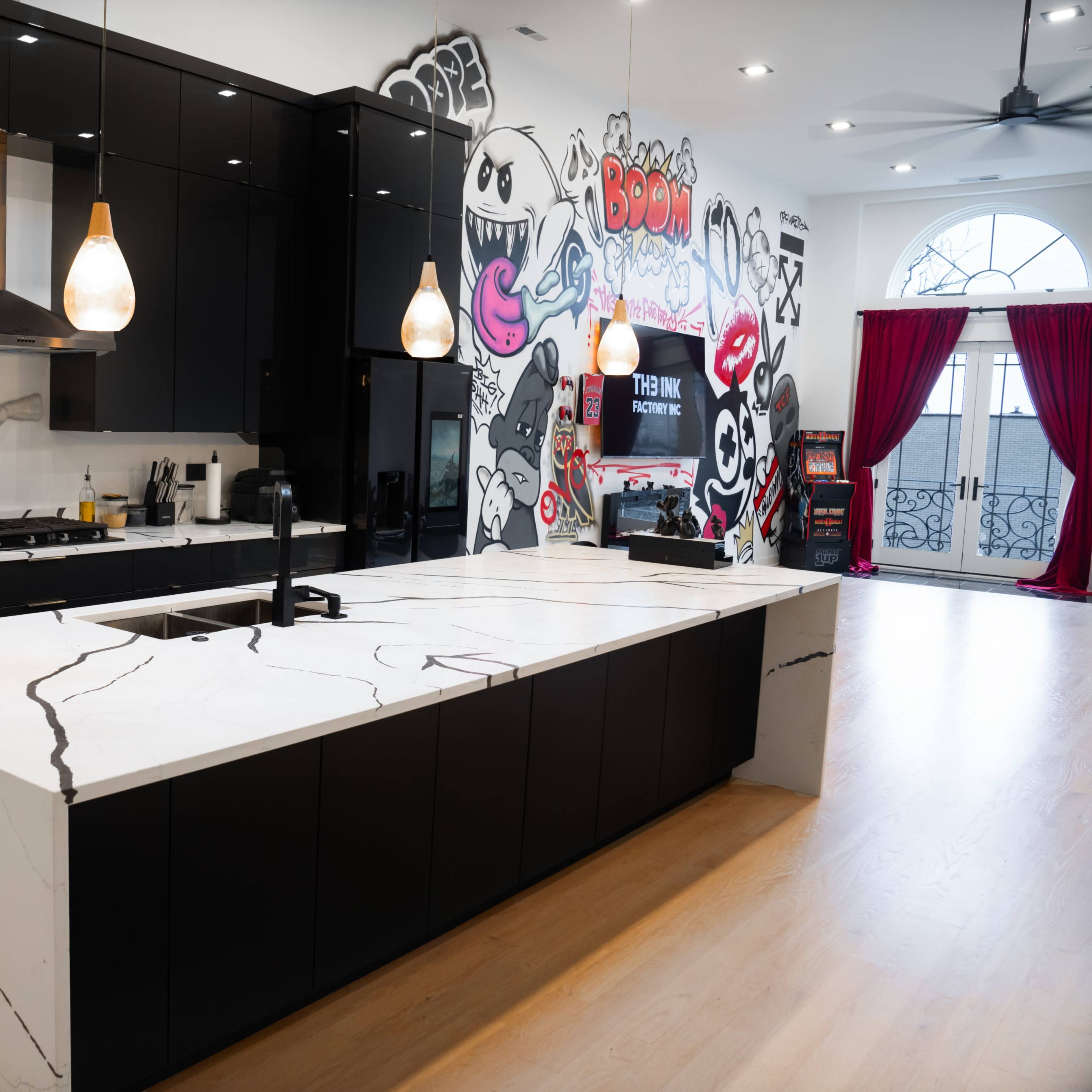 A modern kitchen with black cabinetry, a large marble island, and colorful graffiti artwork on the wall.