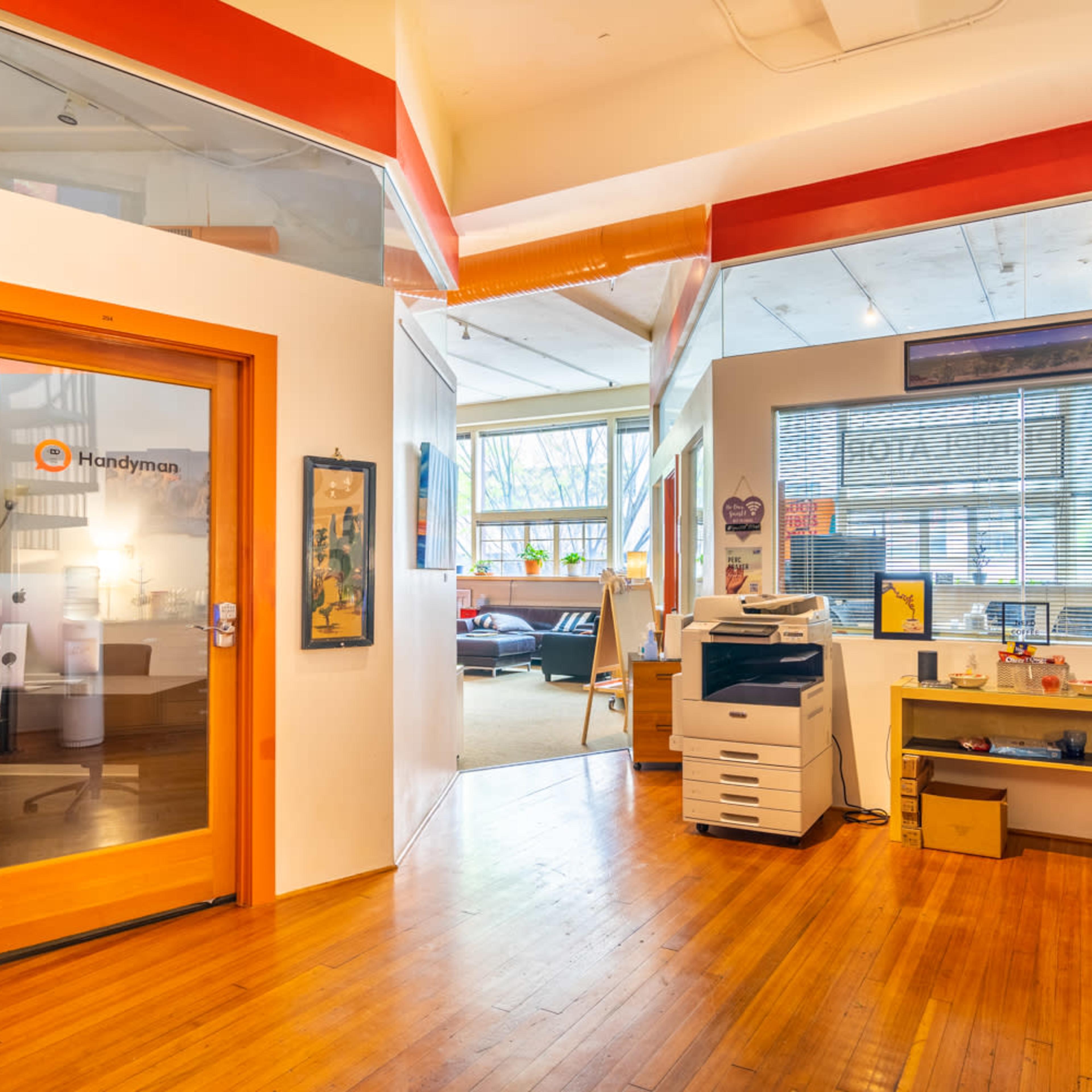 An office space with a glass door labeled "Handyman" leading into a brightly lit room featuring a printer and various decorations.