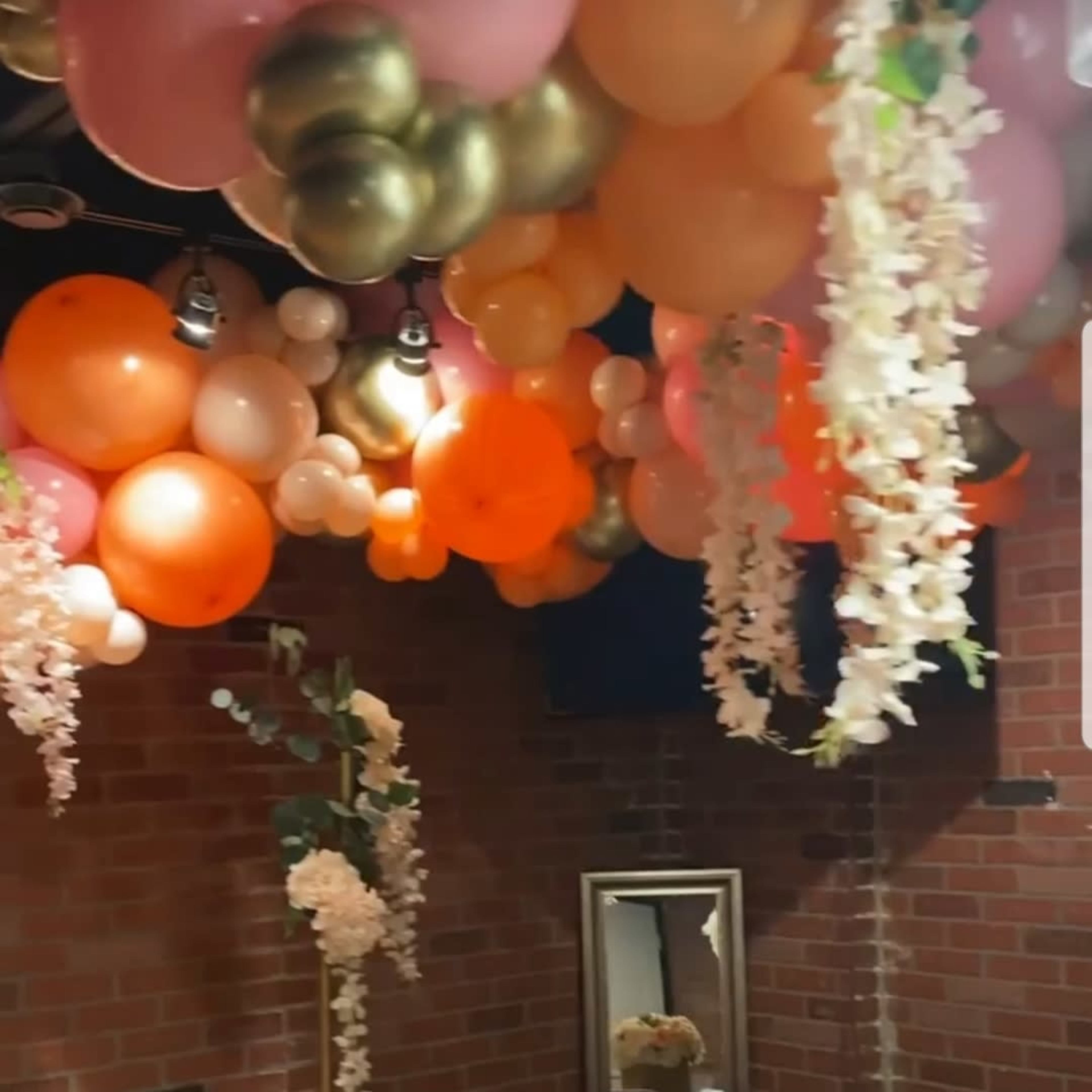 A decorated dining space with a table set for a meal, surrounded by colorful balloons and floral arrangements hanging from the ceiling.